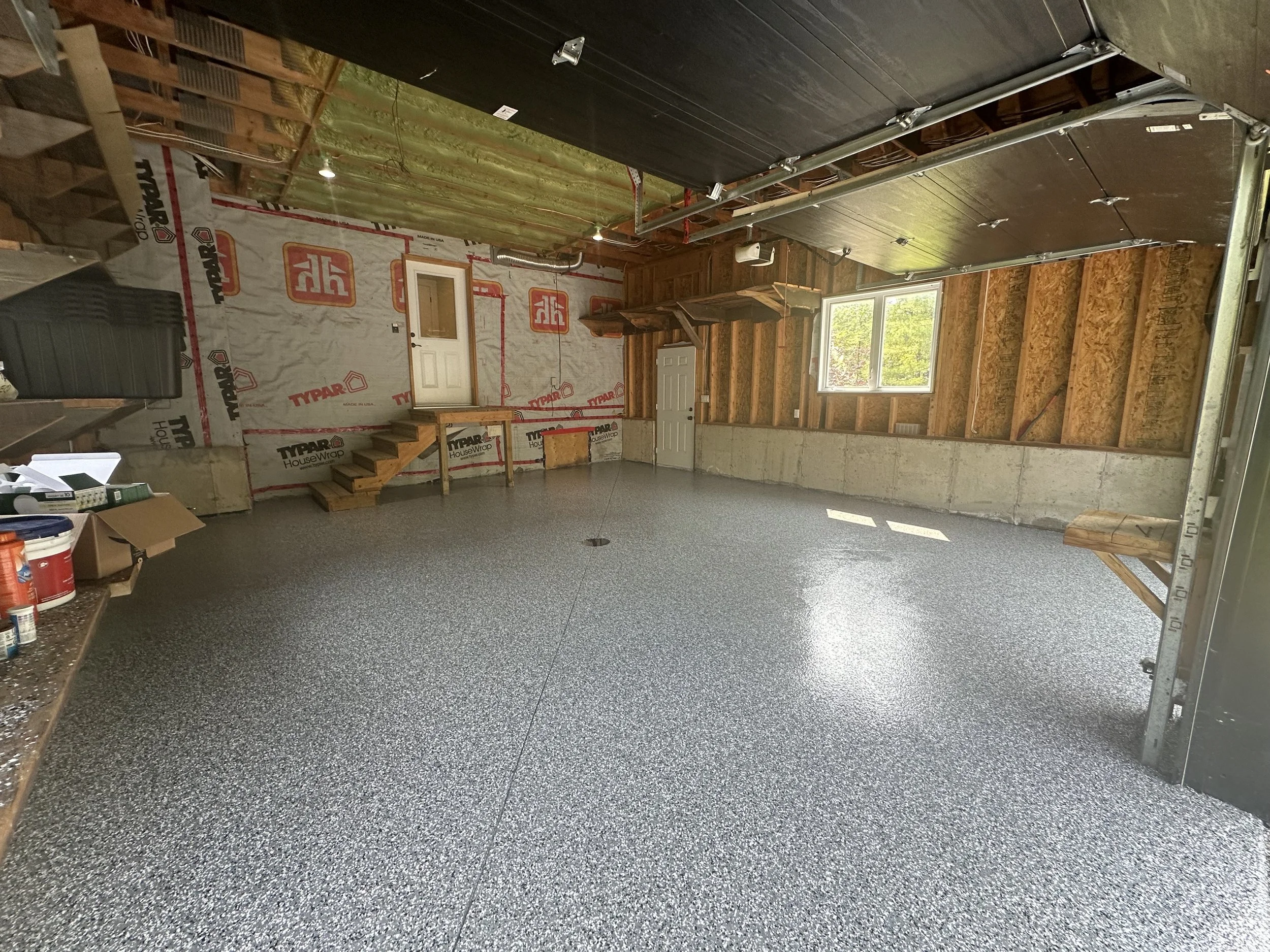 Empty garage with unfinished interior walls, a window, and a freshly installed epoxy floor coating.