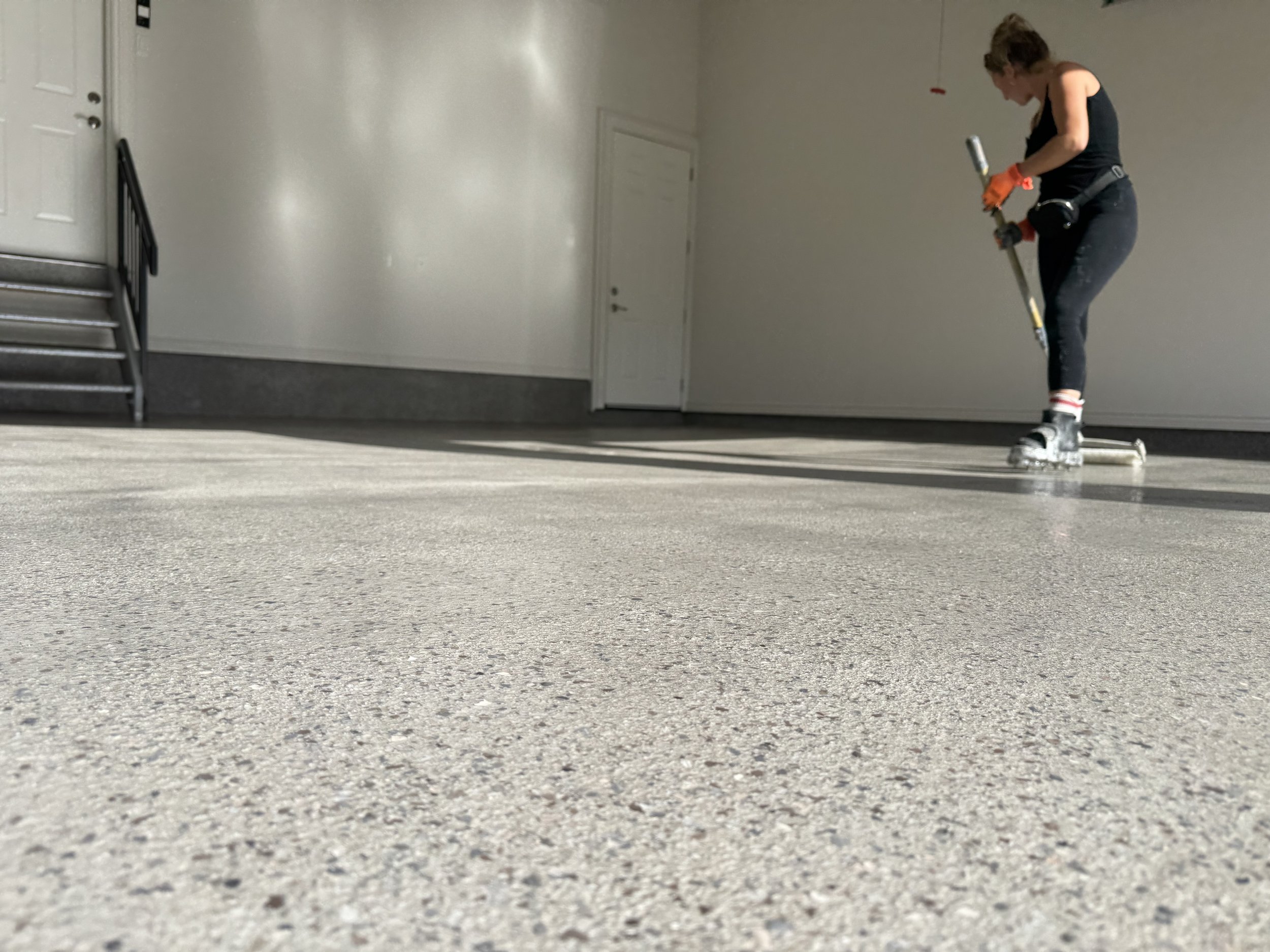 A woman in rollerblades with a power drill in her hands, working on the floor of an empty room.
