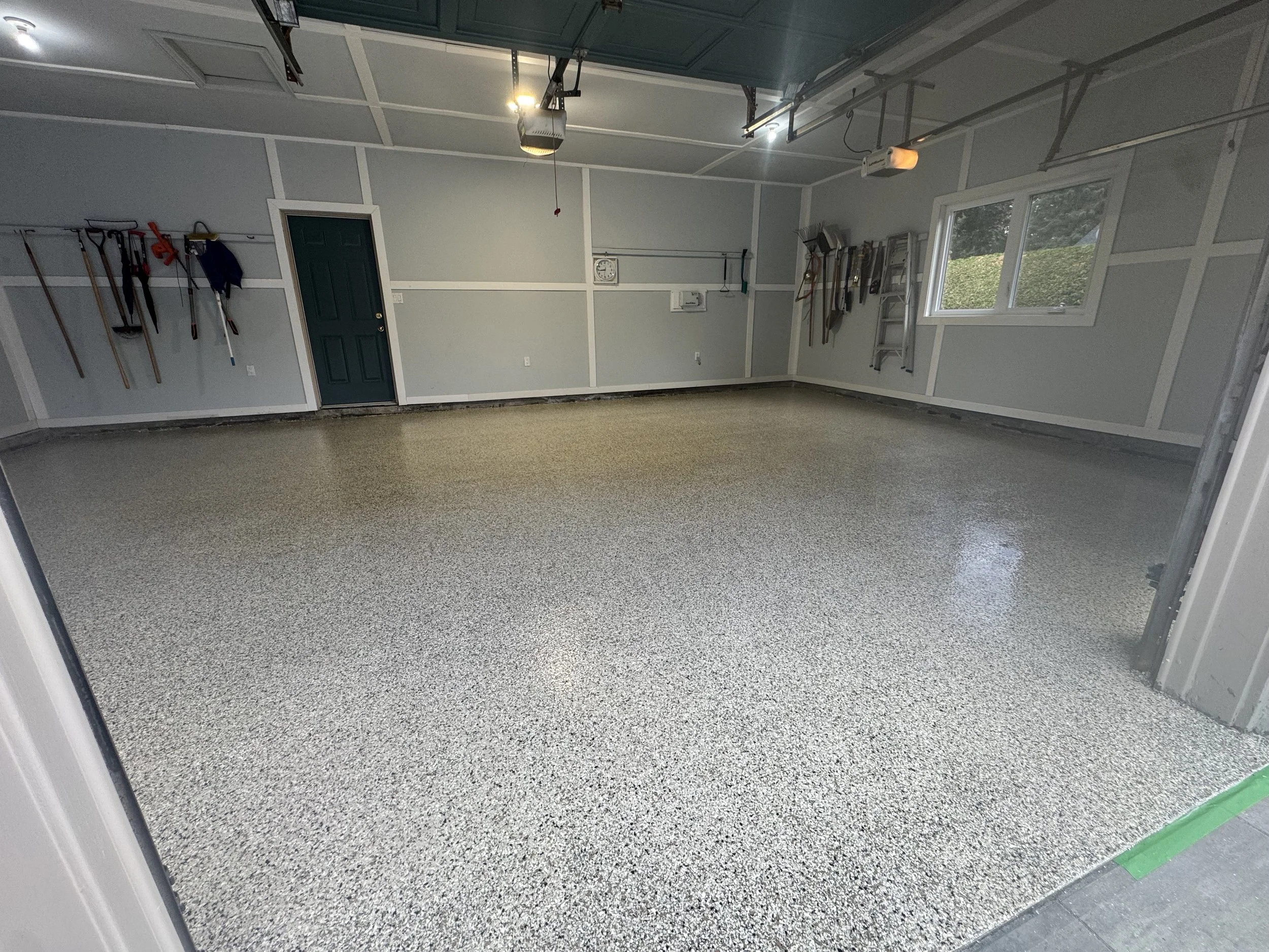 Empty garage with speckled epoxy flooring, tools hanging on the walls, ladder, and a window allowing natural light.