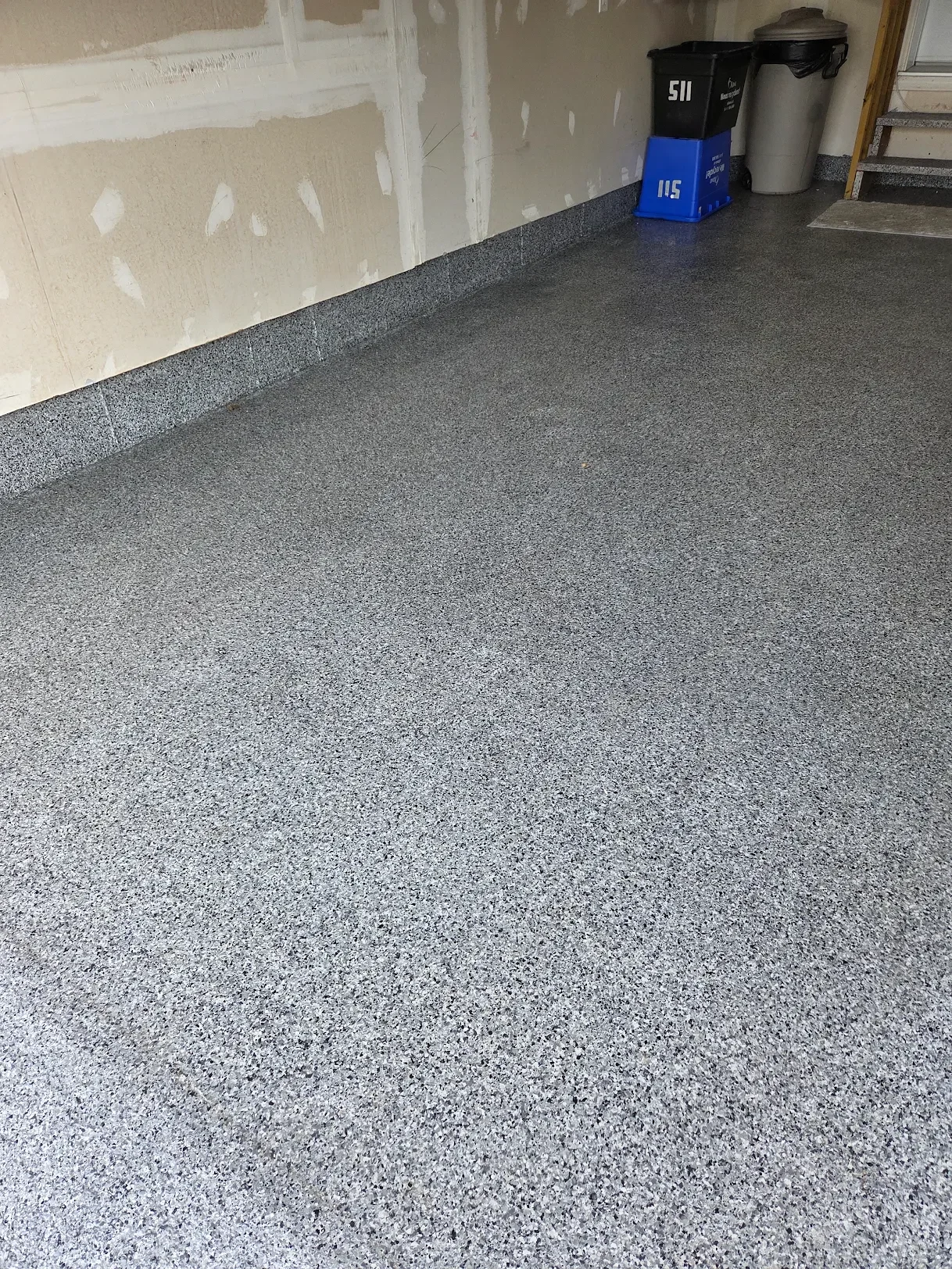Garage with concrete floor, partially finished wall, and trash cans in the corner.