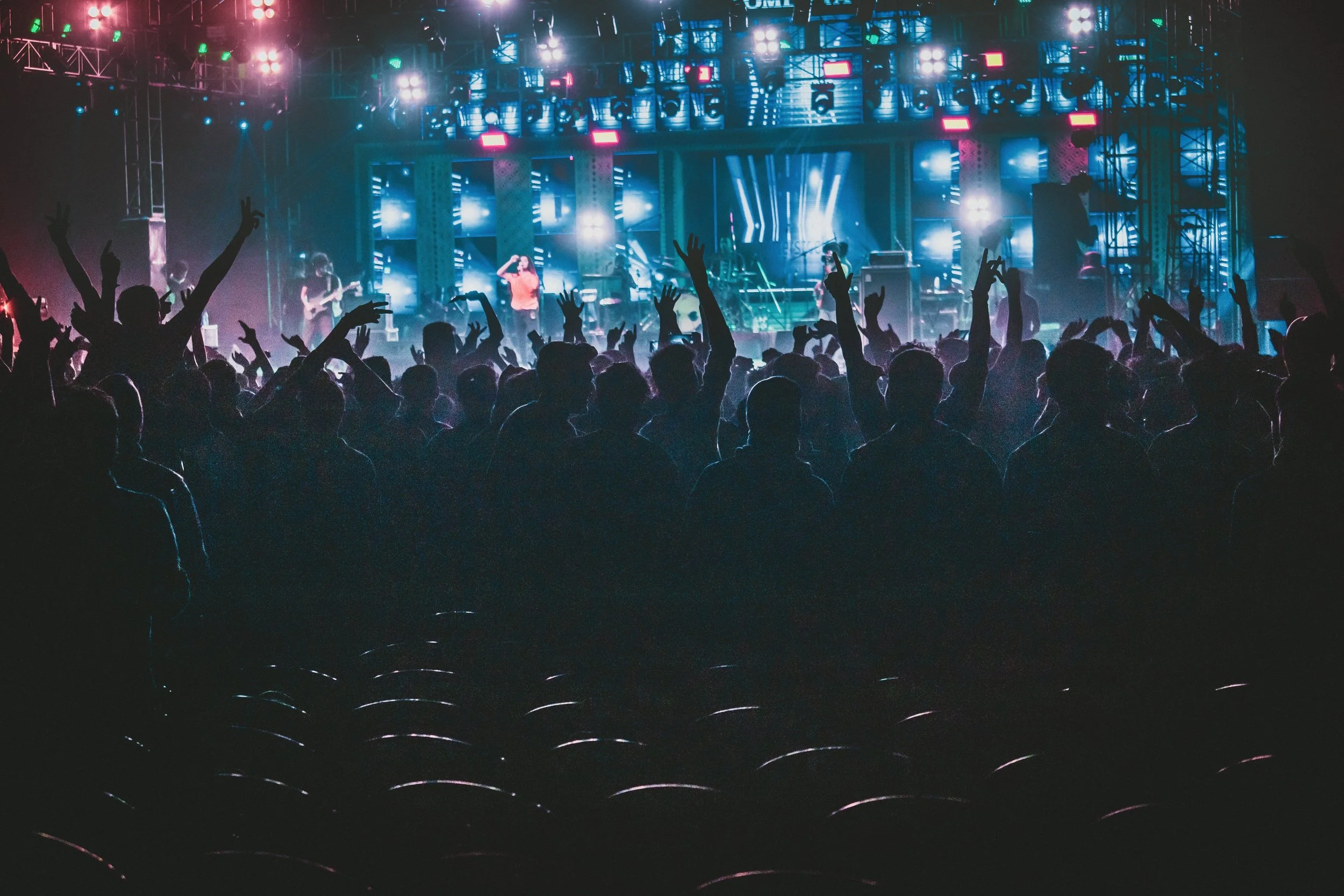 Concierto con público bailando y música en vivo en un escenario iluminado con luces de colores y efectos visuales.