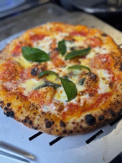 Fresh mozzarella and basil pizza with a slightly charred crust sitting on a metal pizza peel.