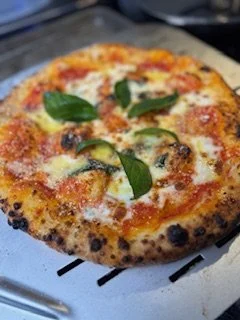 Close-up of a freshly baked Margherita pizza with melted cheese, tomato slices, basil leaves, and a slightly charred crust.
