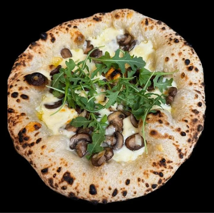 Pizza topped with mushrooms, arugula, and cheese on a black background.
