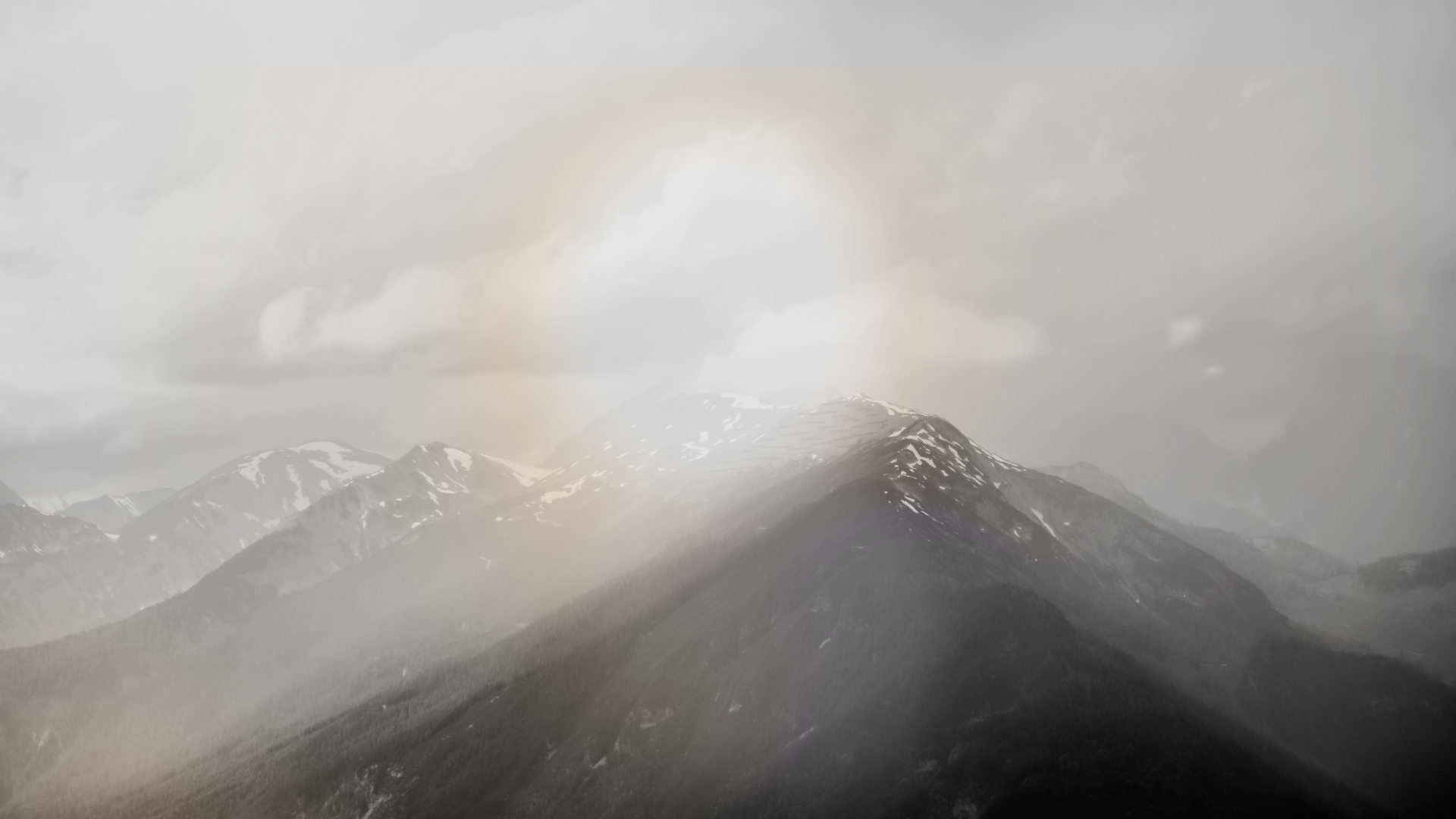 Black and white photo of mountain range with snow-capped peaks under cloudy sky