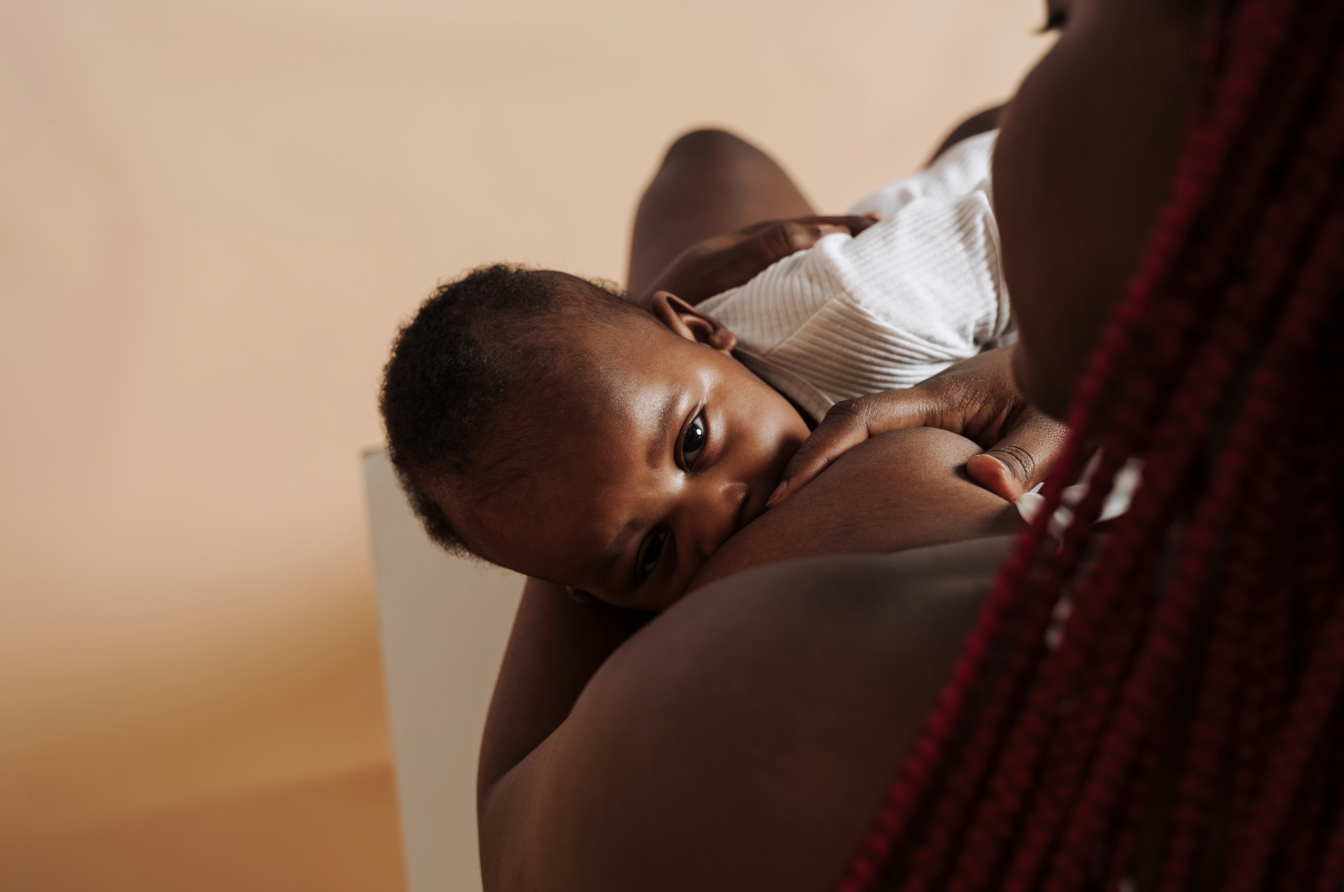 A young child breastfeeding from a woman, lying on her side, with the child's face resting on her chest and hand on her breast.