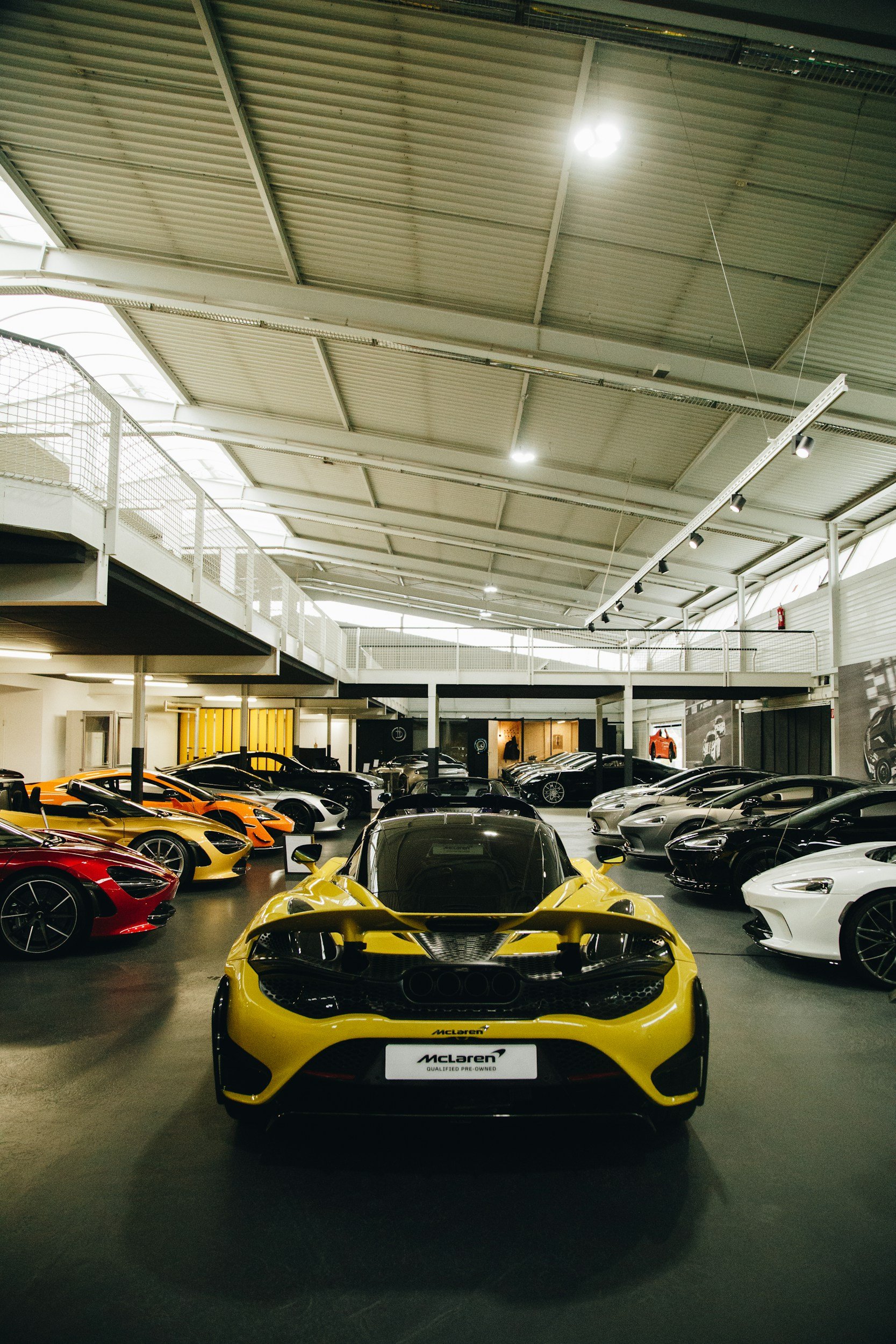 Yellow McLaren sports car in a showroom filled with various colored high-end cars.