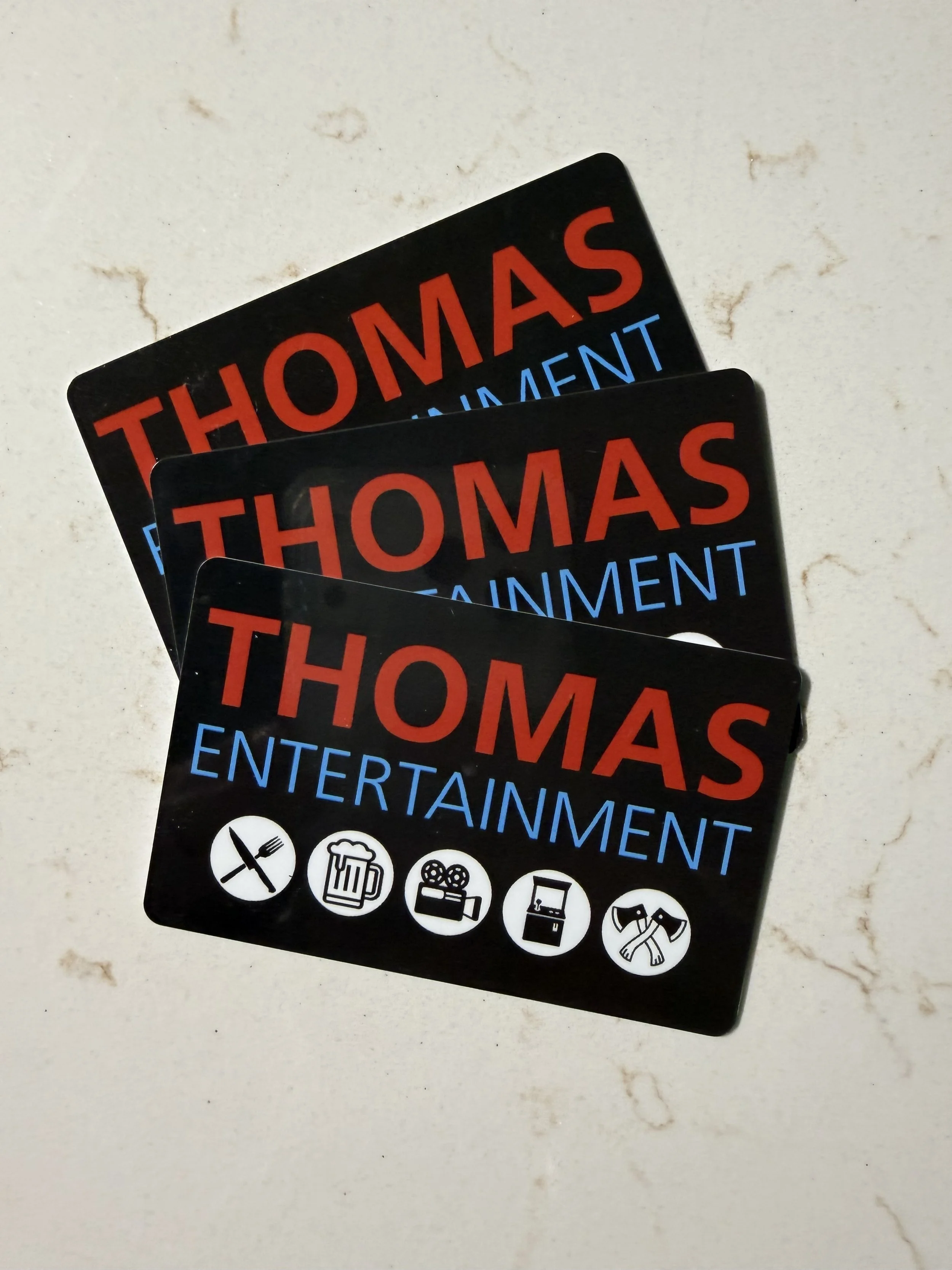 Group of black entertainment cards with red, blue, and white text and icons, placed on a white marble surface.