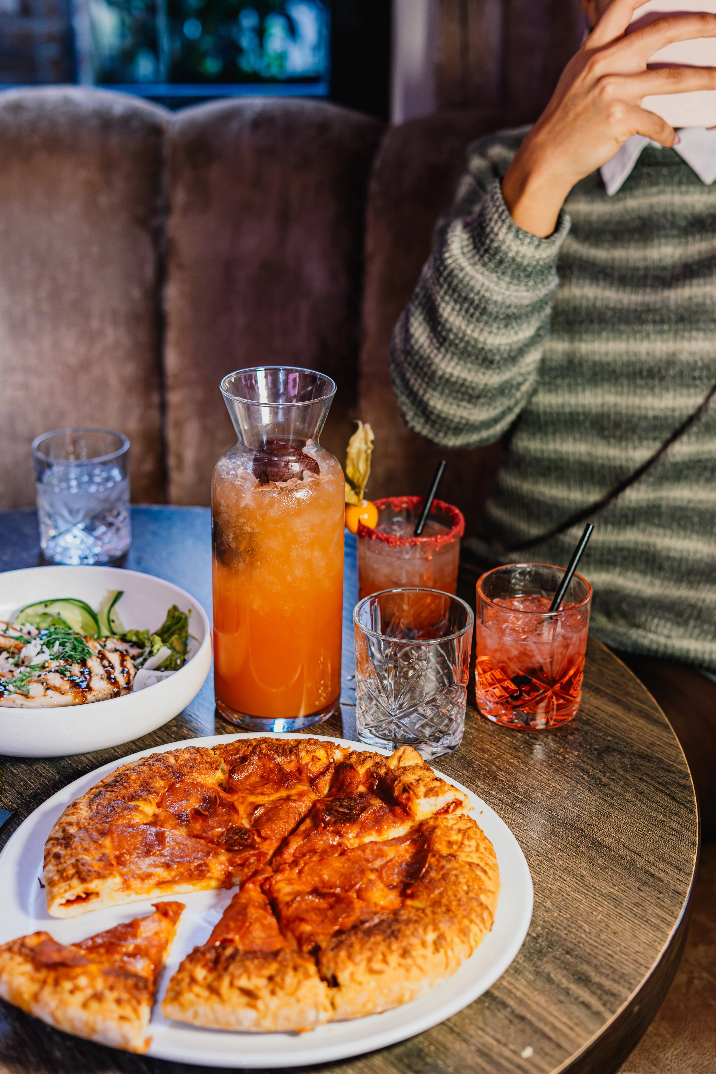 Pizza, drinks, and salad on a wooden table in a restaurant setting.