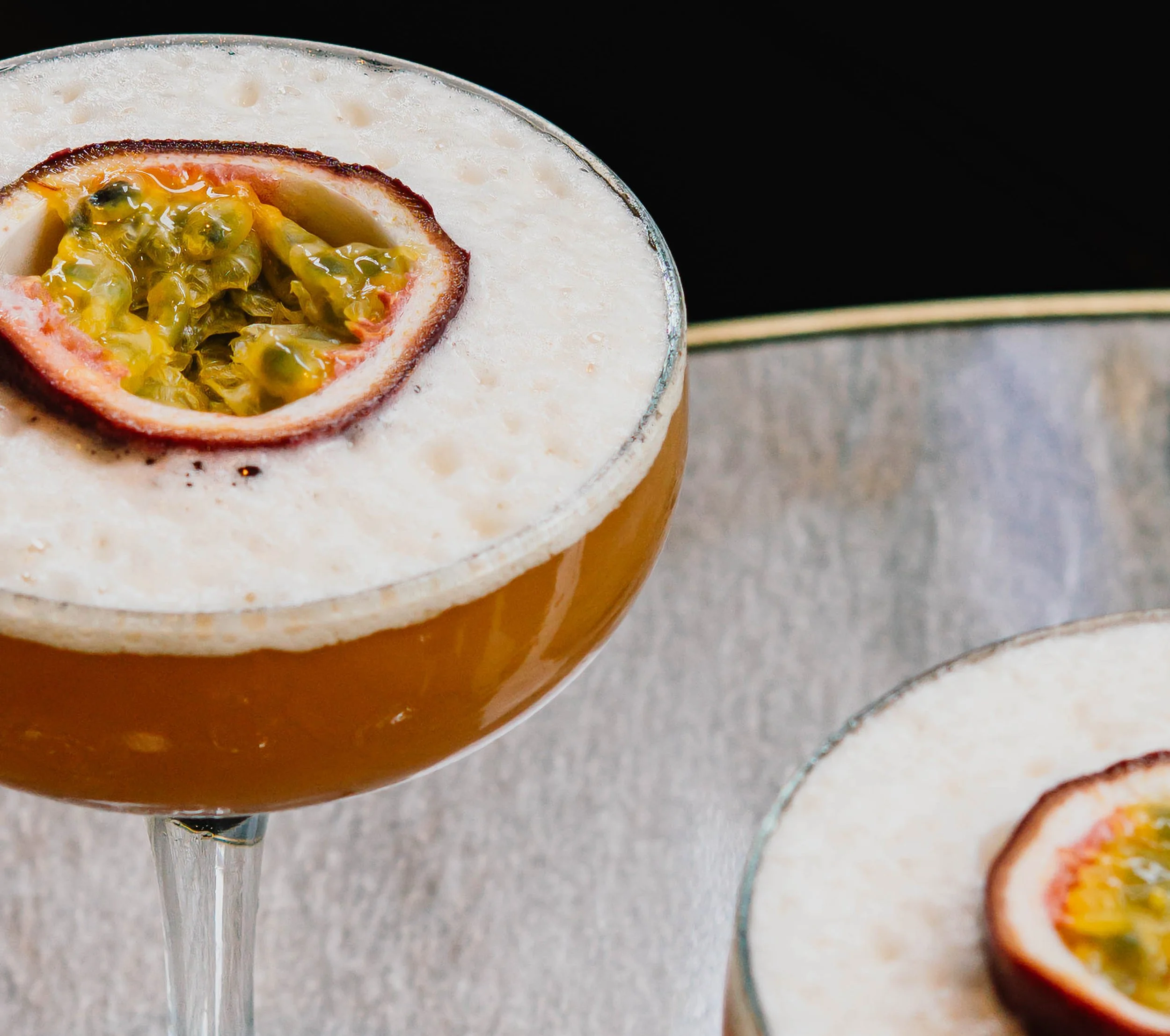 Close-up of a passion fruit cocktail garnished with half passion fruit on the rim of a glass