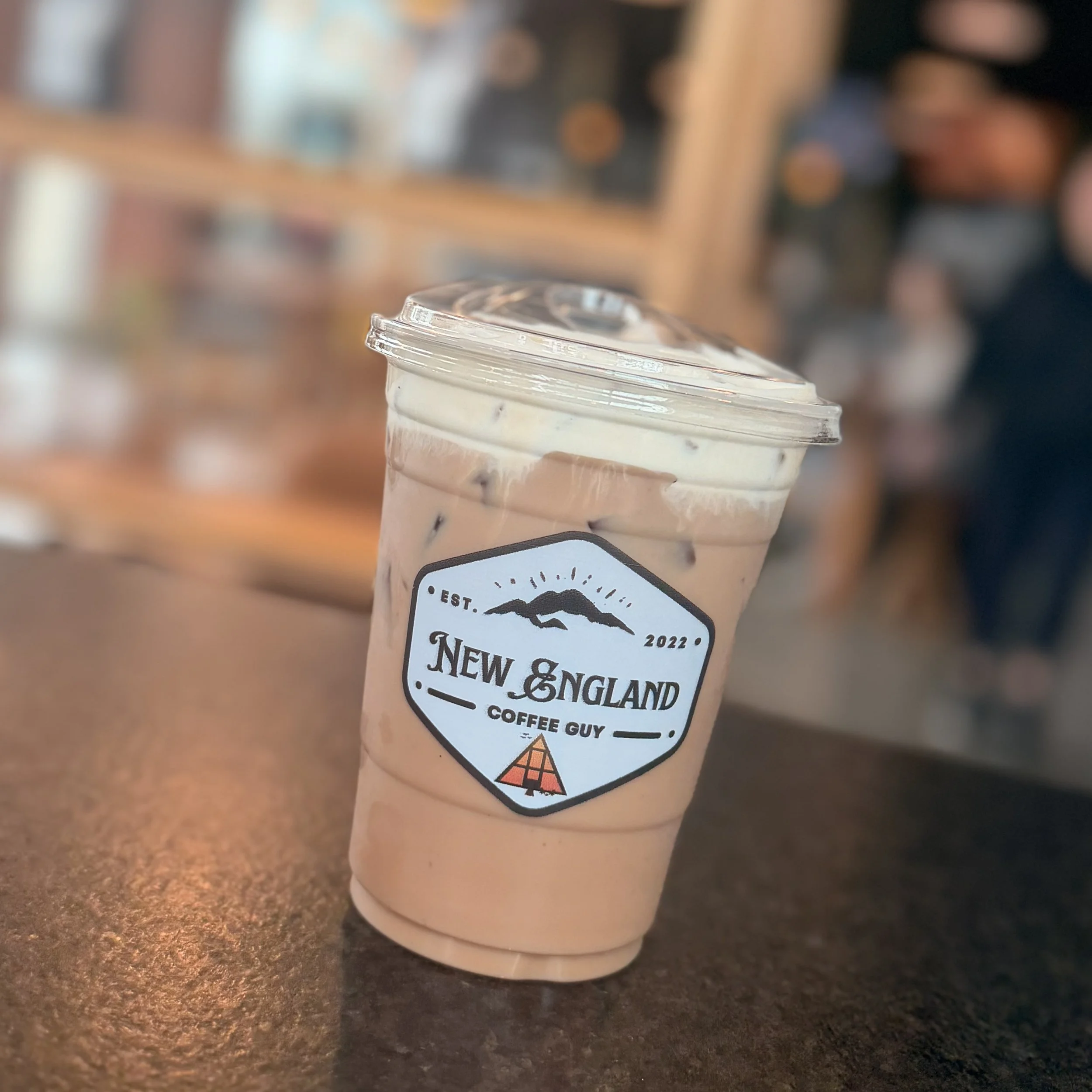A plastic cup filled with a light pink beverage topped with whipped cream, sitting on a dark countertop in a cafe.