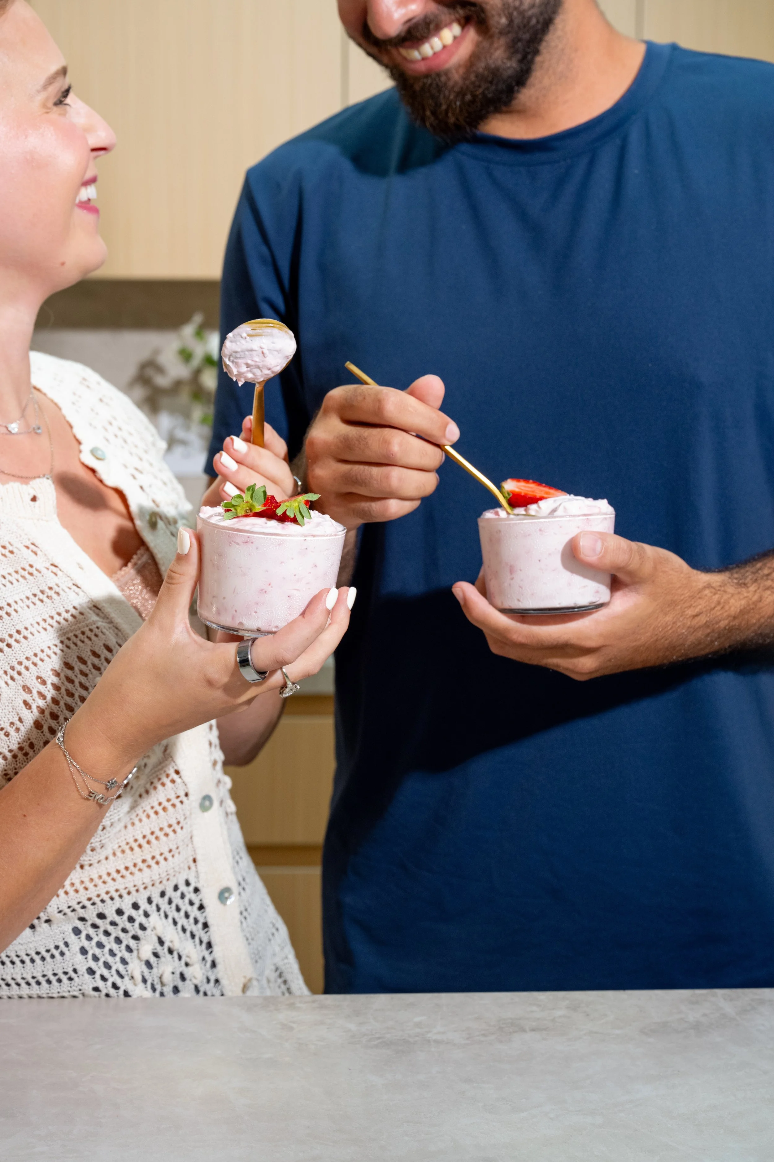 A couple sharing strawberry ice cream sundaes, smiling and enjoying their dessert together in a cozy kitchen.