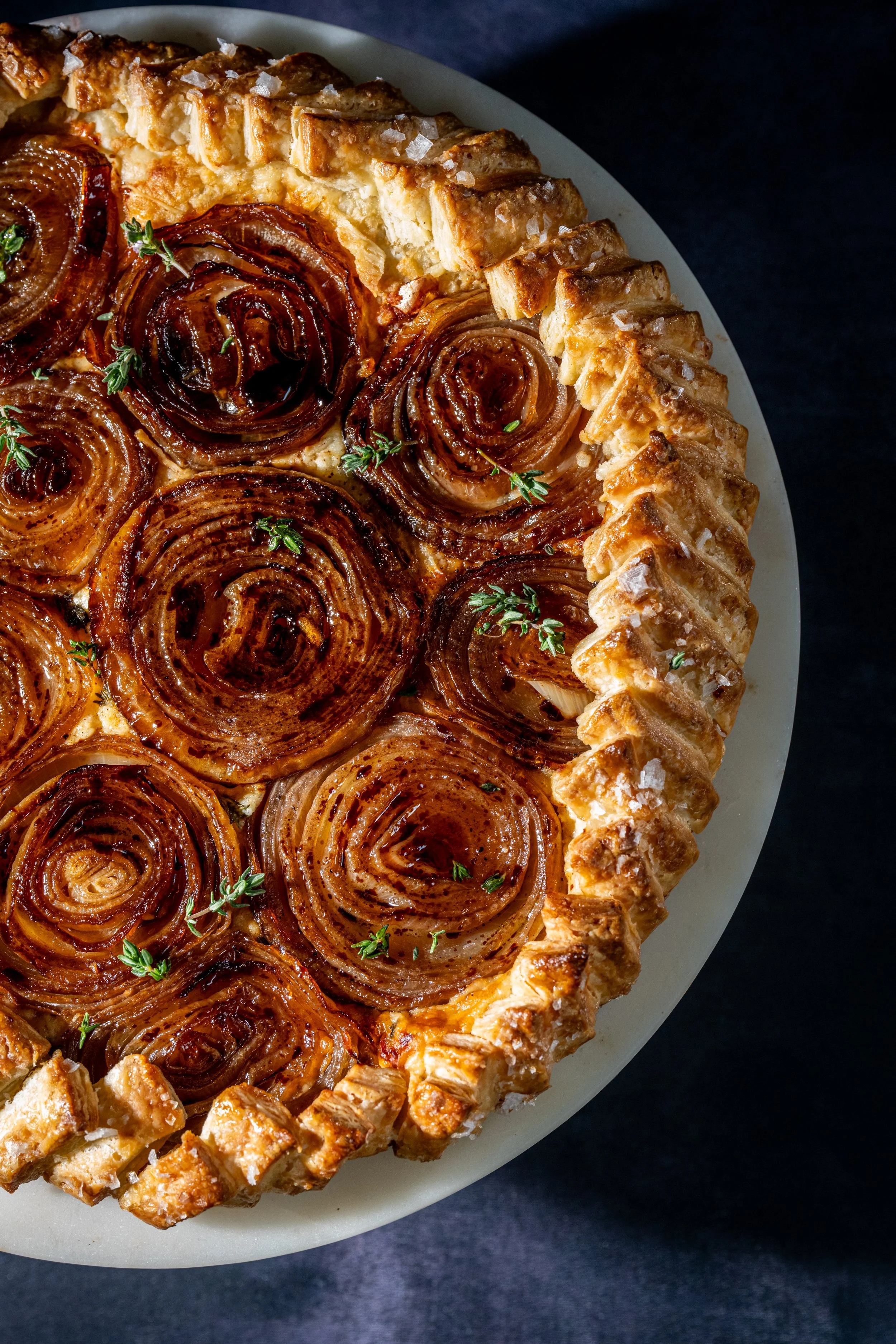 A caramelized onion galette with a flaky crust, garnished with fresh herbs, on a white plate