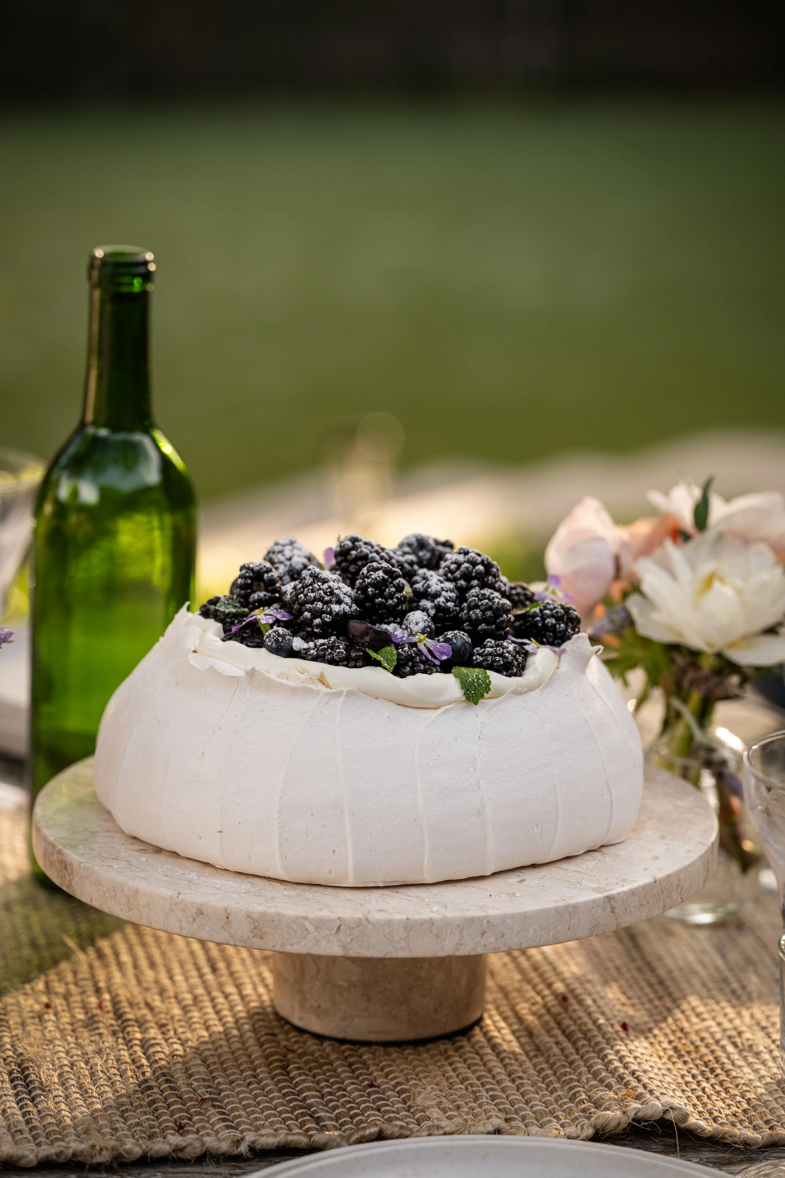 A pavlova dessert topped with blackberries and mint leaves on a marble cake stand.
