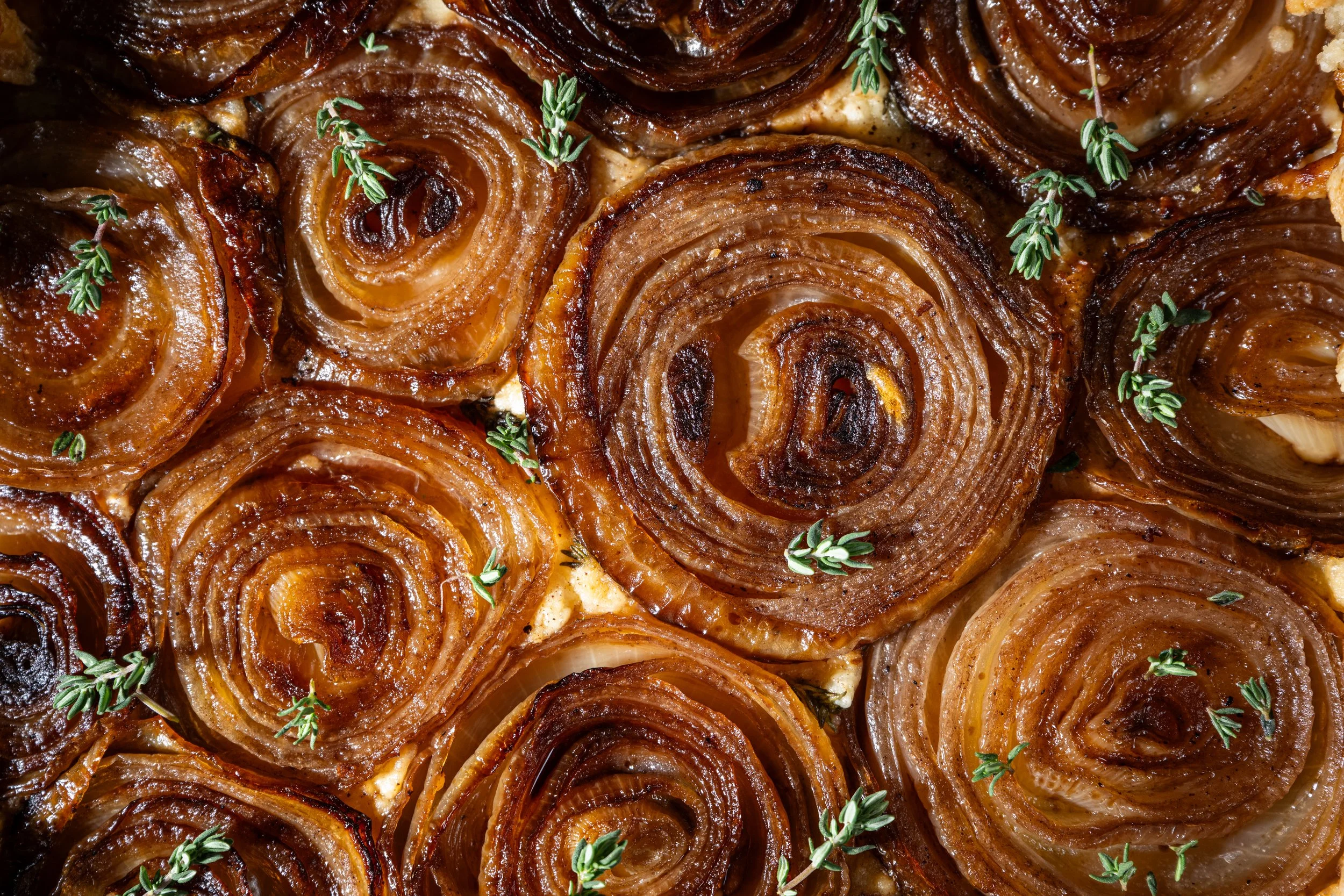 Close-up of caramelized onion roses garnished with small green herbs.