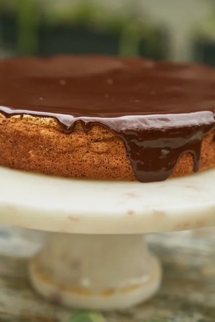 Chocolate glaze on a round cake with a textured brown crust, resting on a white cake stand.