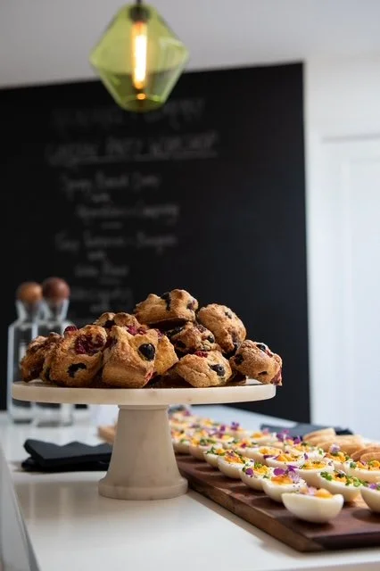 A white cake stand holding a pile of mixed berry scones or muffins in a kitchen with chalkboard and festive treats in the background.