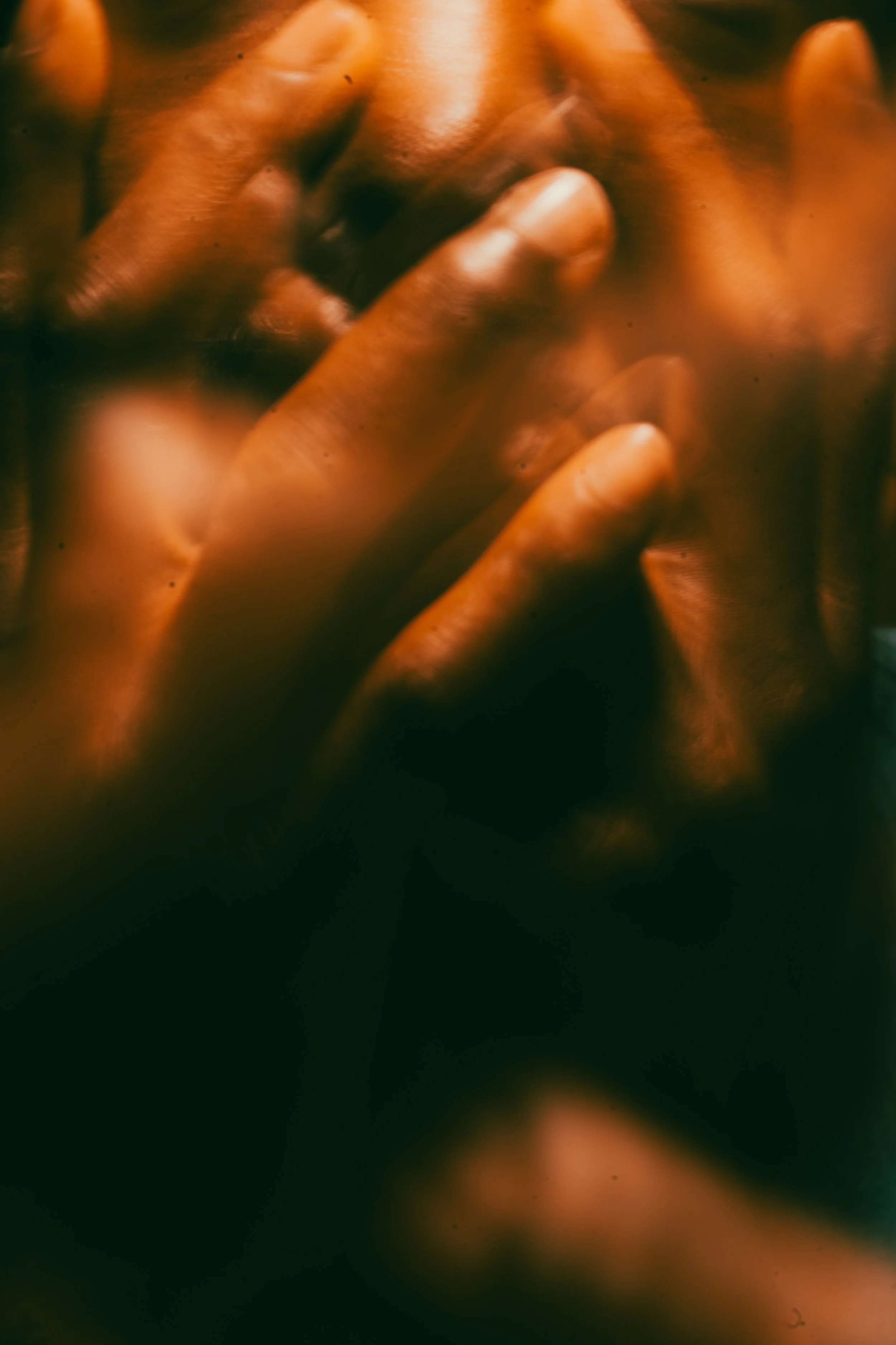 Close-up of a person's hands clasped together with fingers intertwined, in a dimly lit setting with warm tones.