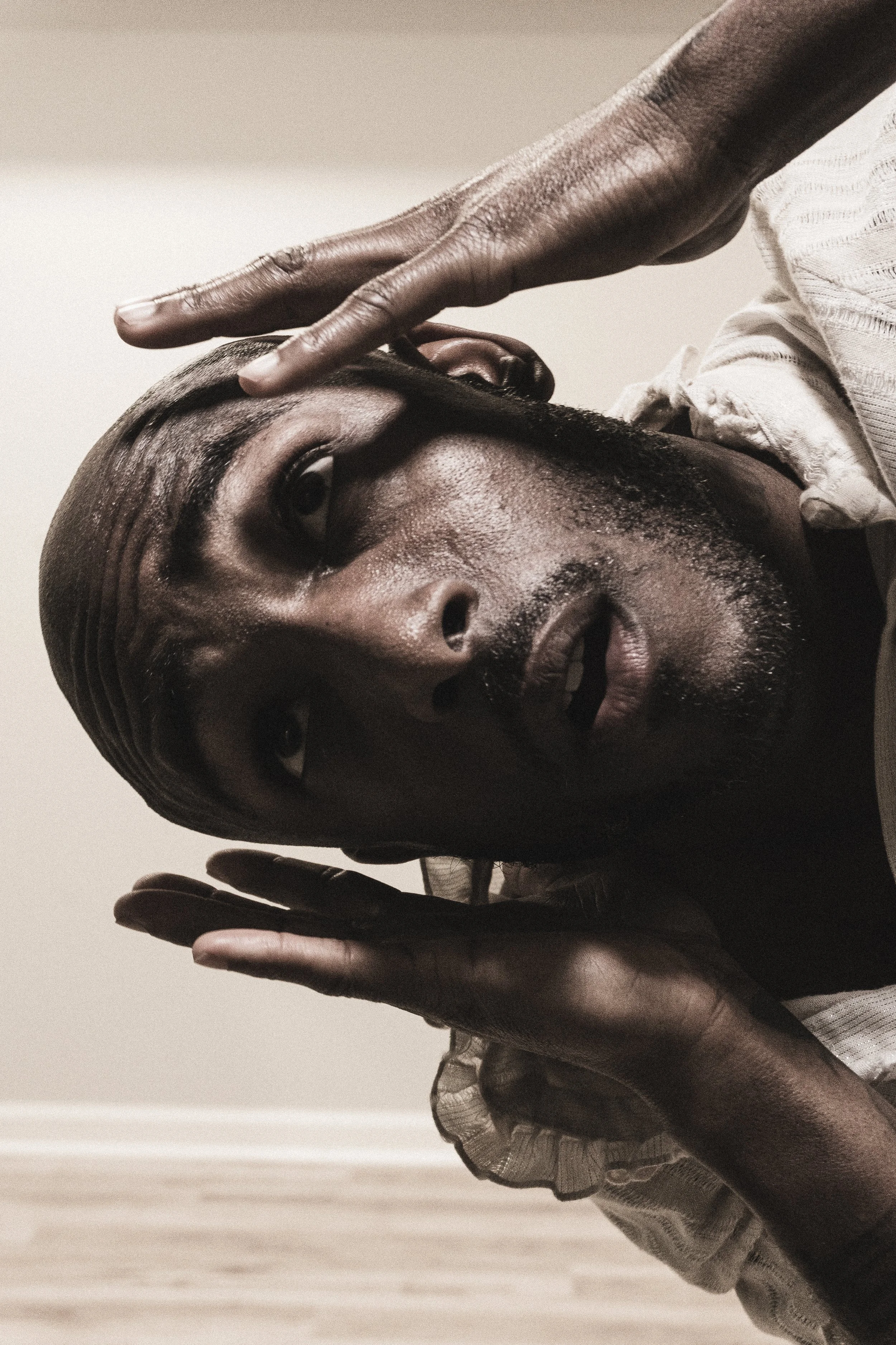 A close-up of a man with dark skin touching his forehead with his hand, expressing a contemplative or emotional moment.