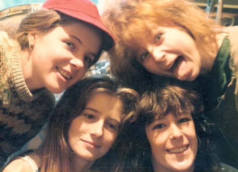 Four young women smiling and posing closely together for a selfie, outdoors at night.
