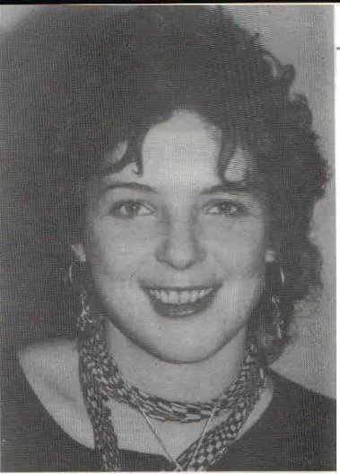 Black and white photo of a smiling woman with curly hair, wearing earrings and layered necklaces.