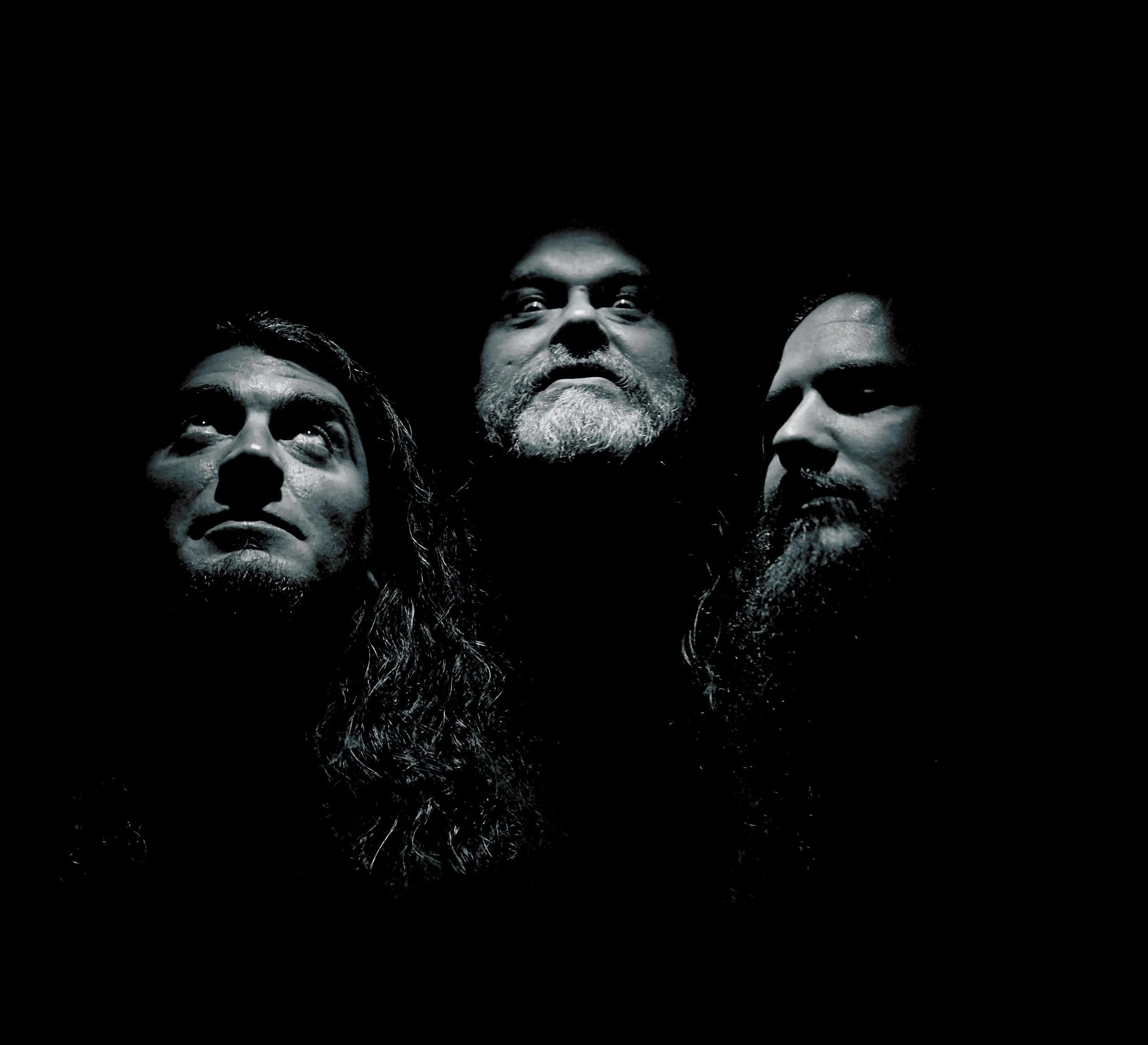 Close-up of three people's faces with only their heads visible against a black background, looking upward.