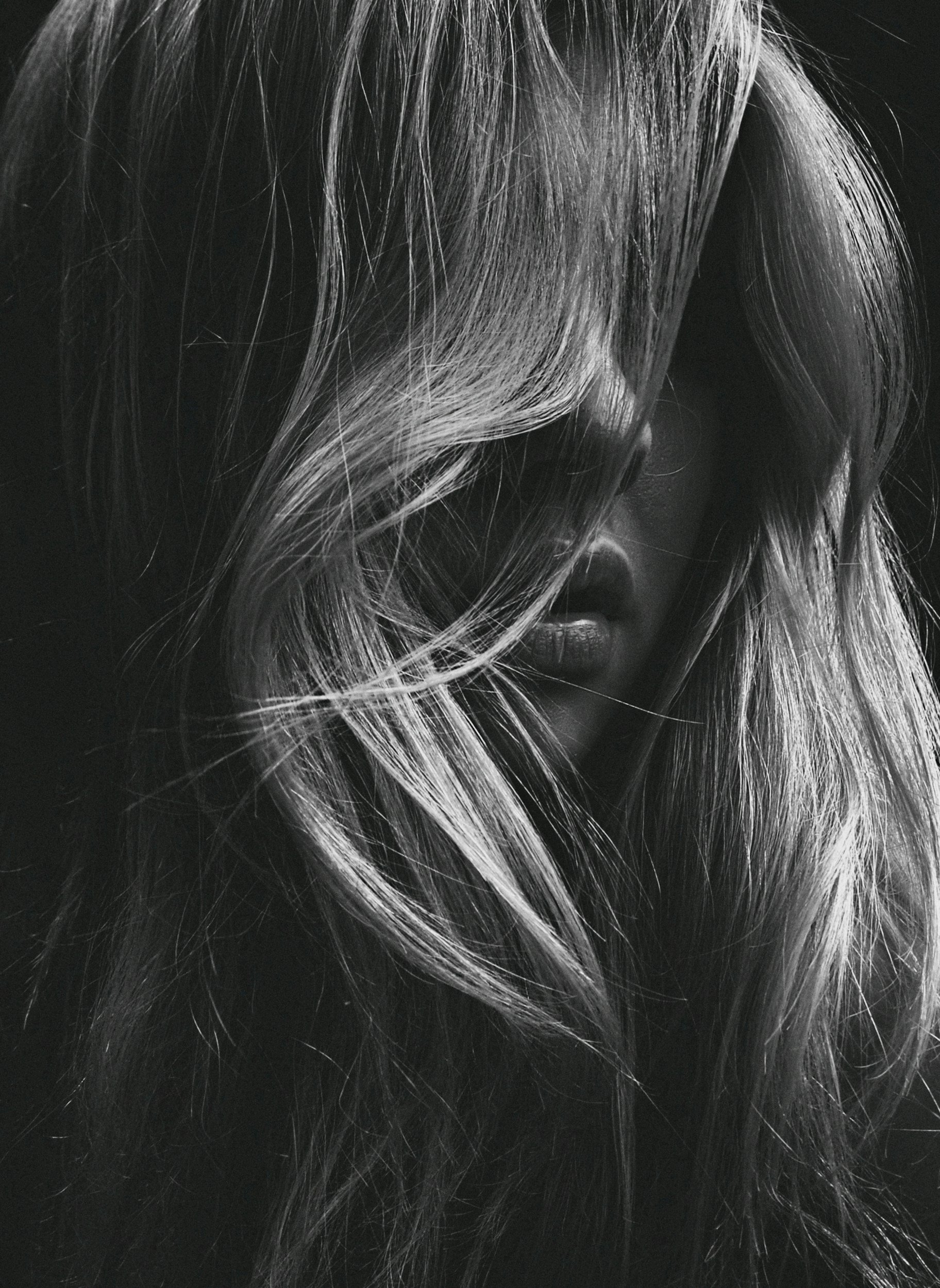 Close-up of flowing light-colored hair and partially visible face on a dark background.