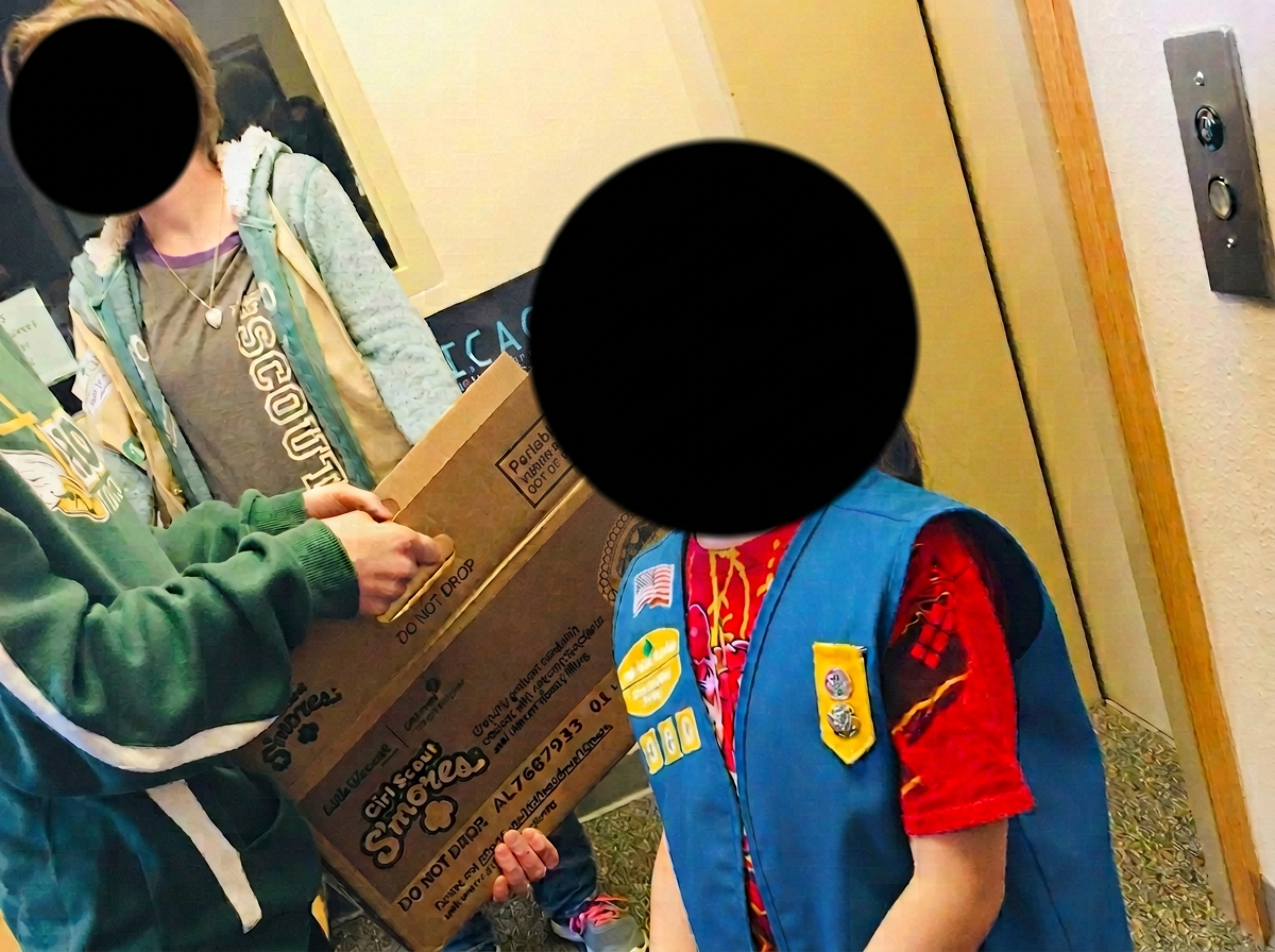 Girl Scout wearing a patch-covered uniform indoors, with her face blurred for privacy.