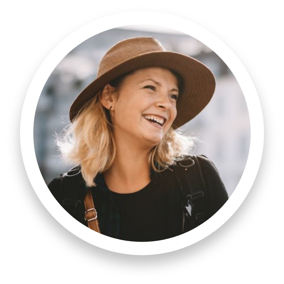 A woman in a brown wide-brimmed hat smiling outdoors, wearing a black top and a backpack.