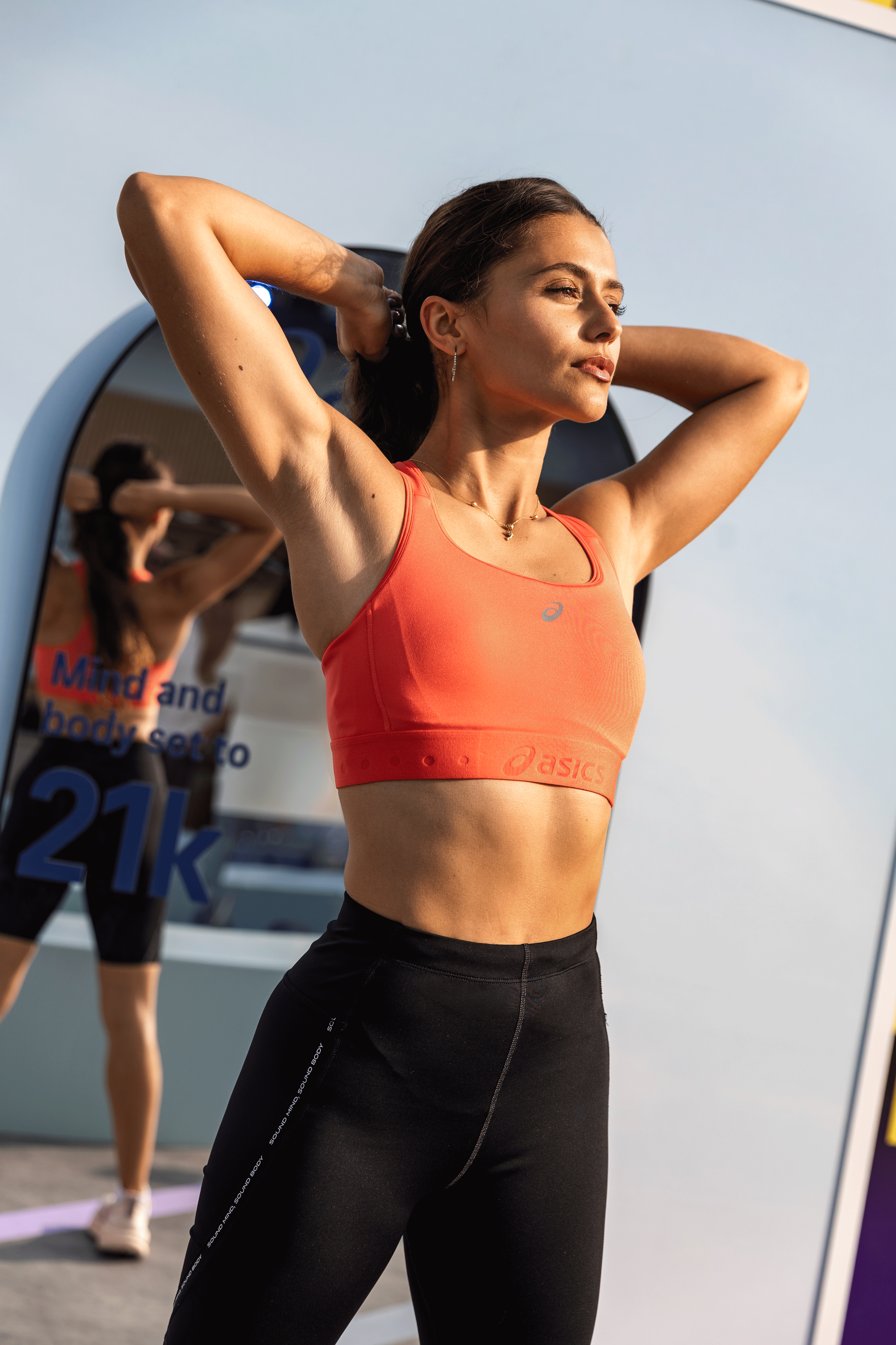 ASICS SPORT PHOTOGRAPHY BY KYNDA CREATIVE IN DUBAI. A woman in sportswear stretching outdoors with a mirror behind her showing her reflection.