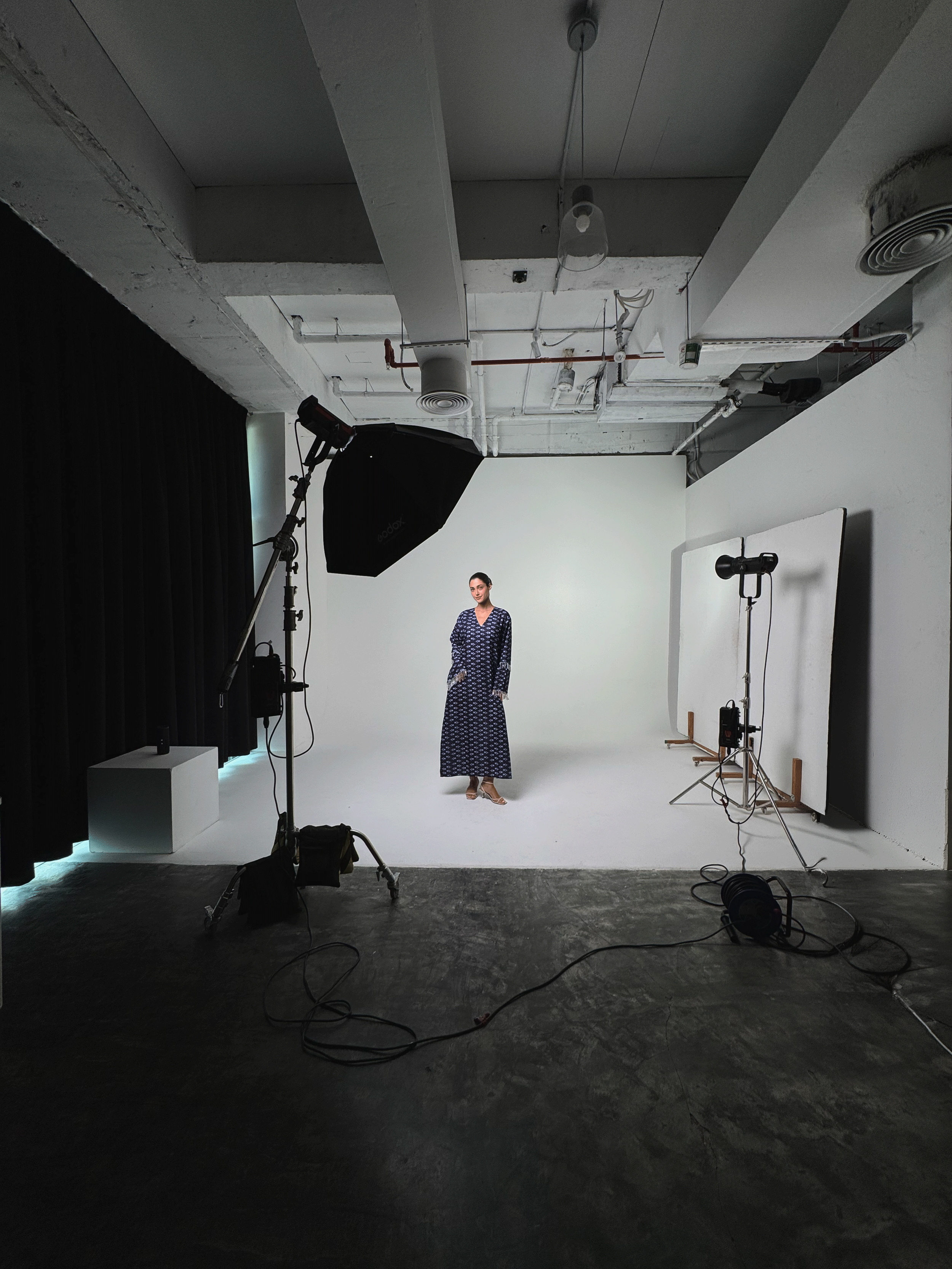 BEHIND THE SCENES OF VIDEO PRODUCTION BY KYNDA CREATIVE IN DUBAI. A woman standing in a photography studio with a white background, professional lighting, and recording equipment.