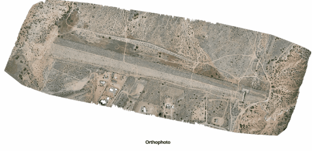 Aerial view of a small airport runway with surrounding buildings and vegetation.