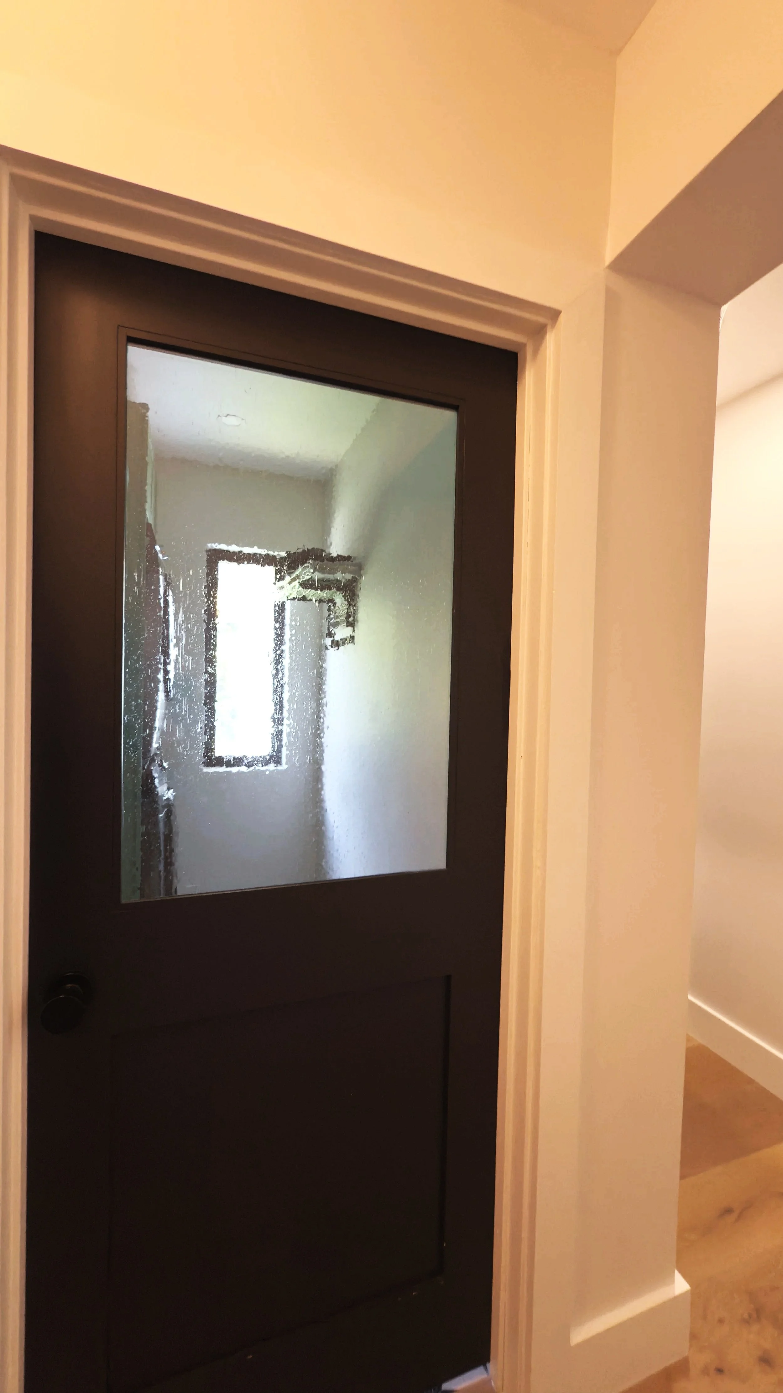 A black interior door with a frosted glass panel, being cleaned or possibly foggy, with a white door frame and beige or off-white walls surrounding it.