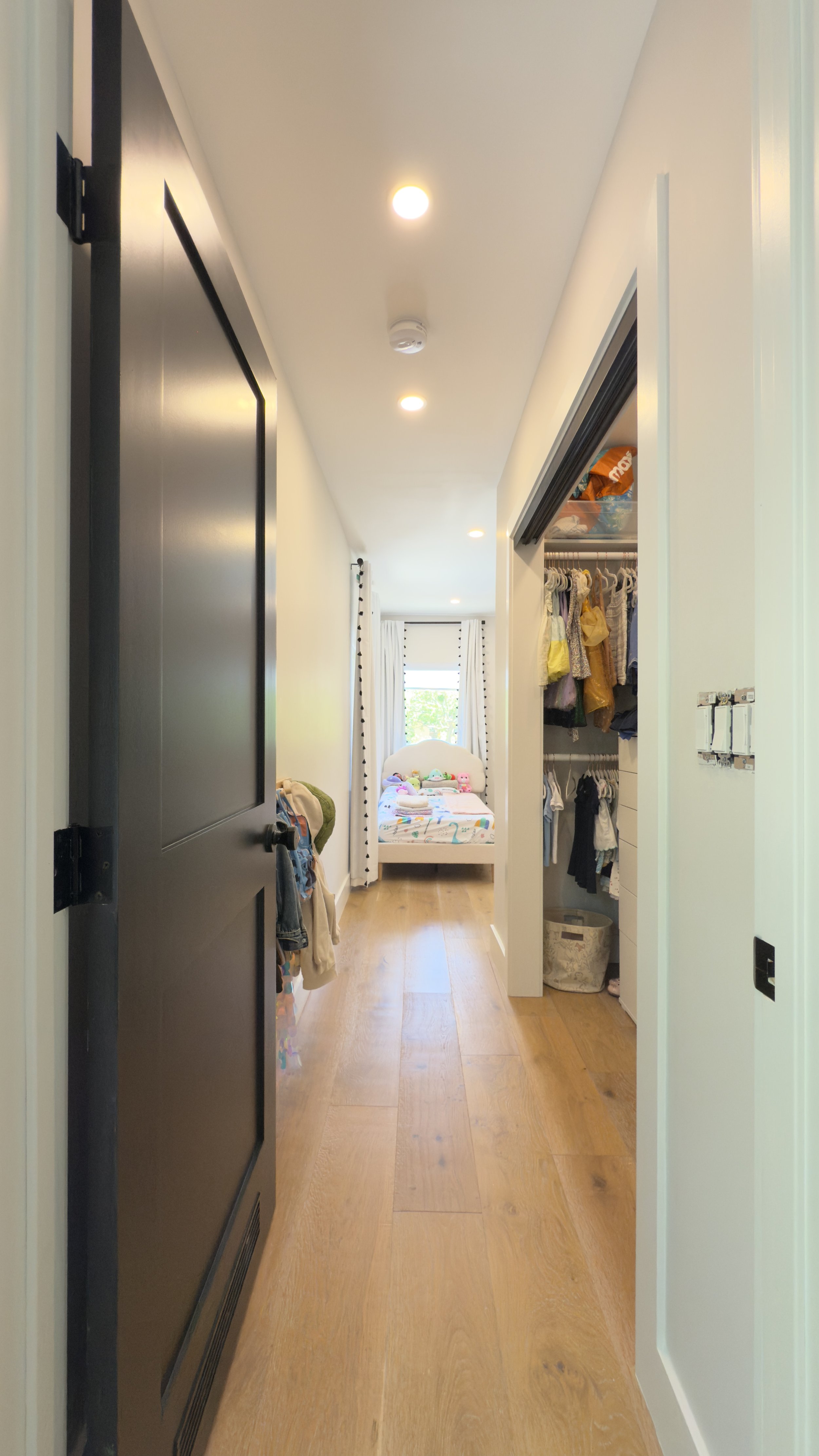 View of a hallway leading to a bedroom with a small bed, decorated with stuffed animals, at the far end of the room.
