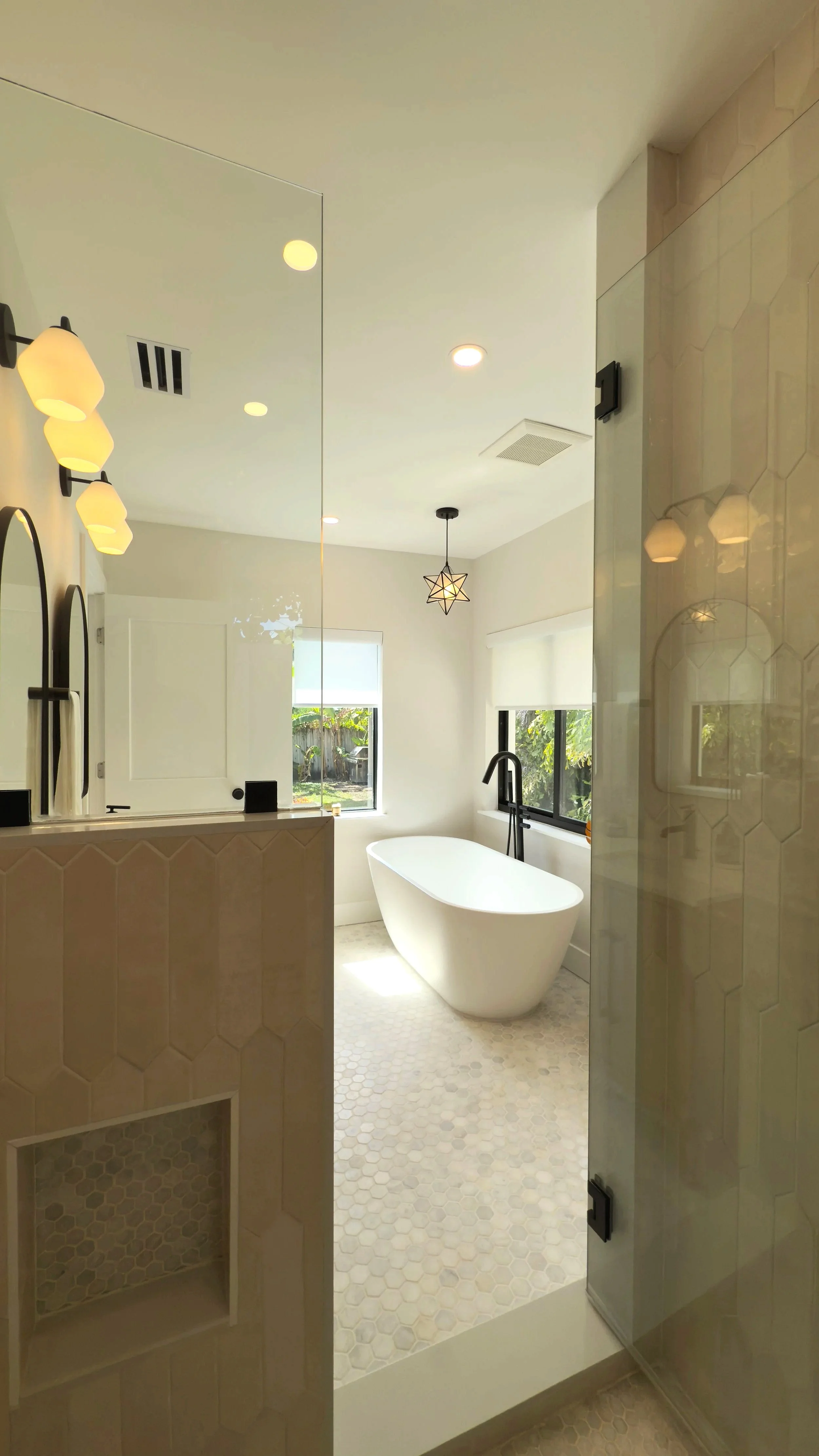Modern bathroom with a white freestanding bathtub near a window, black faucet, hexagon tile flooring, and a star-shaped pendant light.