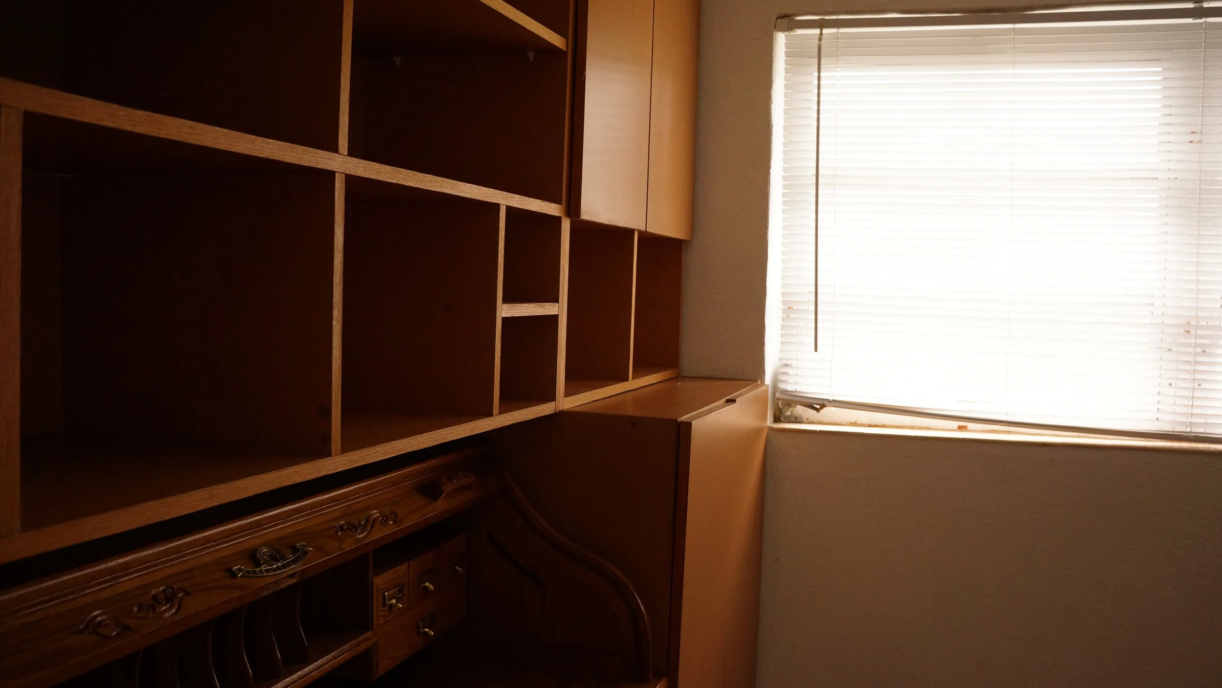 Empty wooden shelving unit with window blinds in a room.