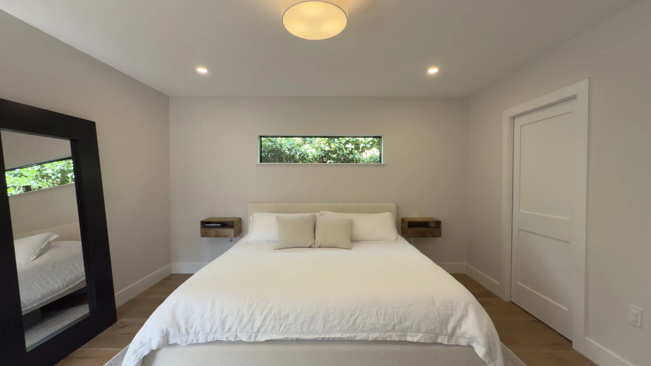 Minimalist bedroom with white bed, small window showing greenery, and floating nightstands