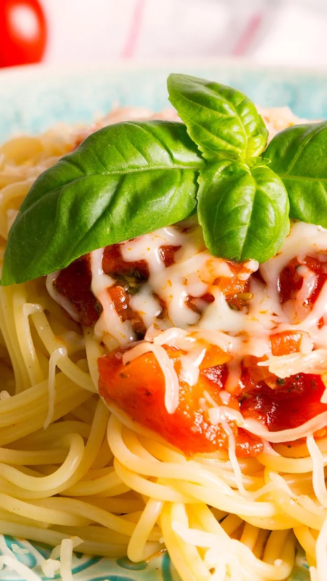 Close-up of spaghetti with tomato sauce, melted cheese, and basil leaves on top.