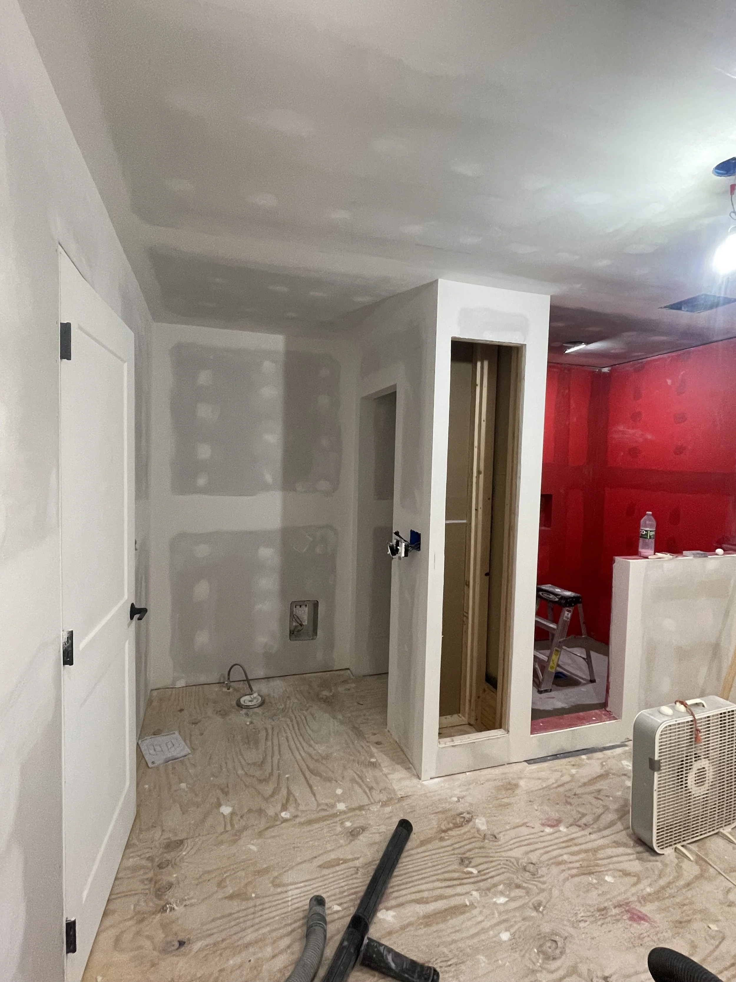 Interior view of a room under construction, with unfinished walls, a red wall, and construction tools on the floor.