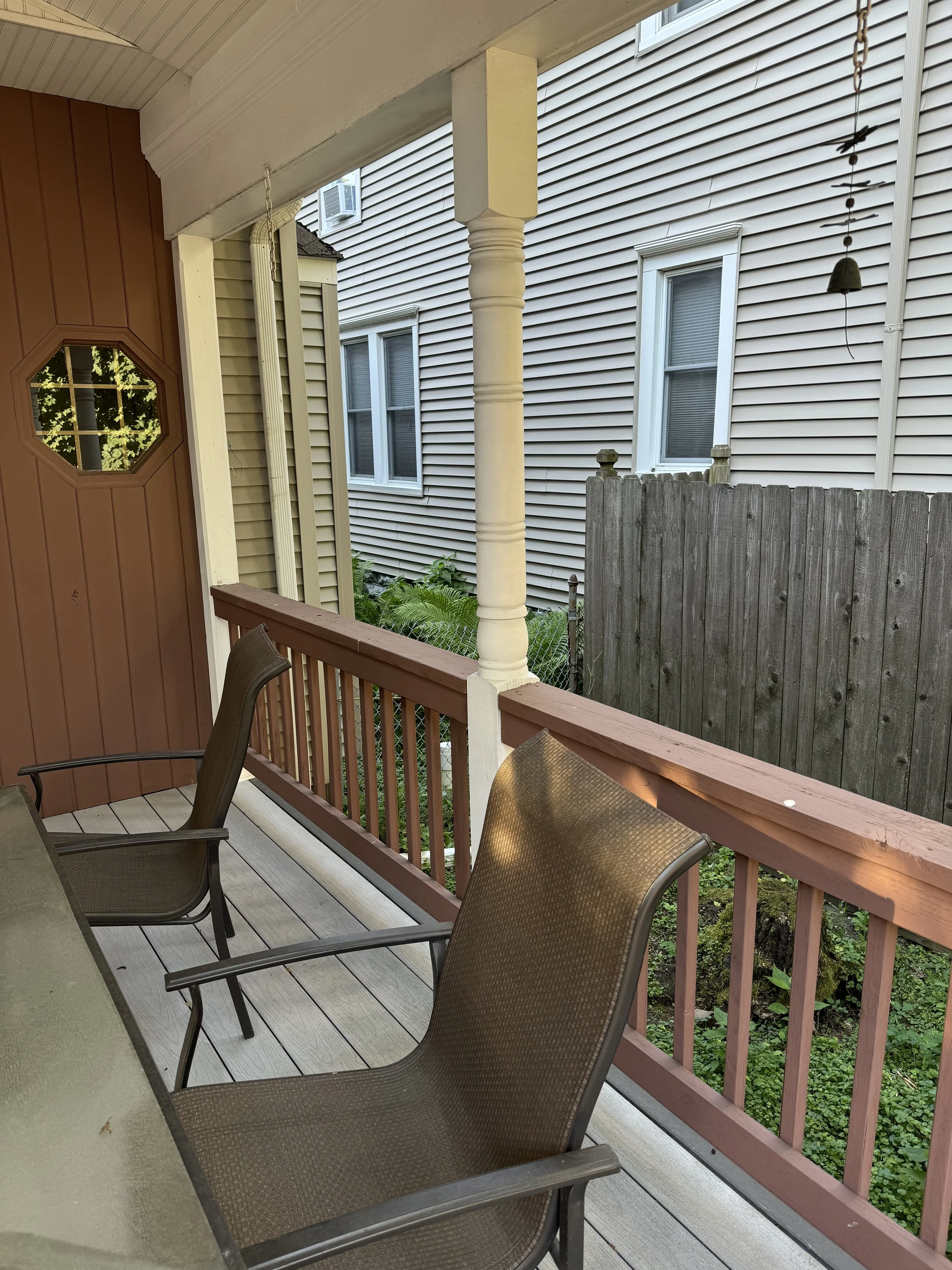 Outdoor porch with two brown mesh chairs, a railing, and a view of neighboring house with beige siding and three windows.