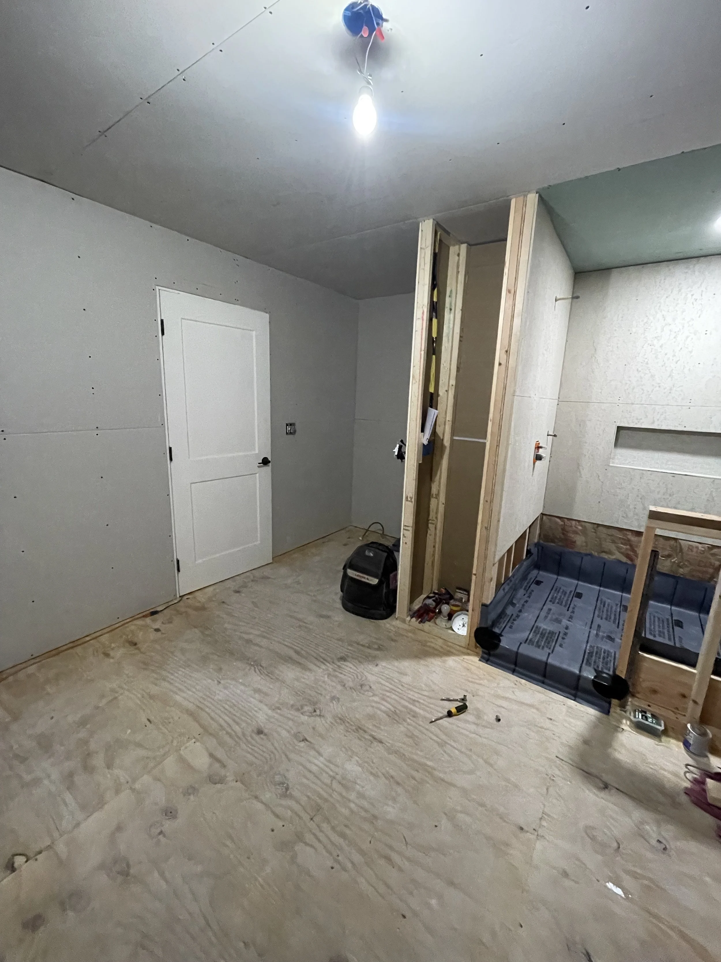 Room under construction with unfinished drywall, a door, tools, and exposed framing.
