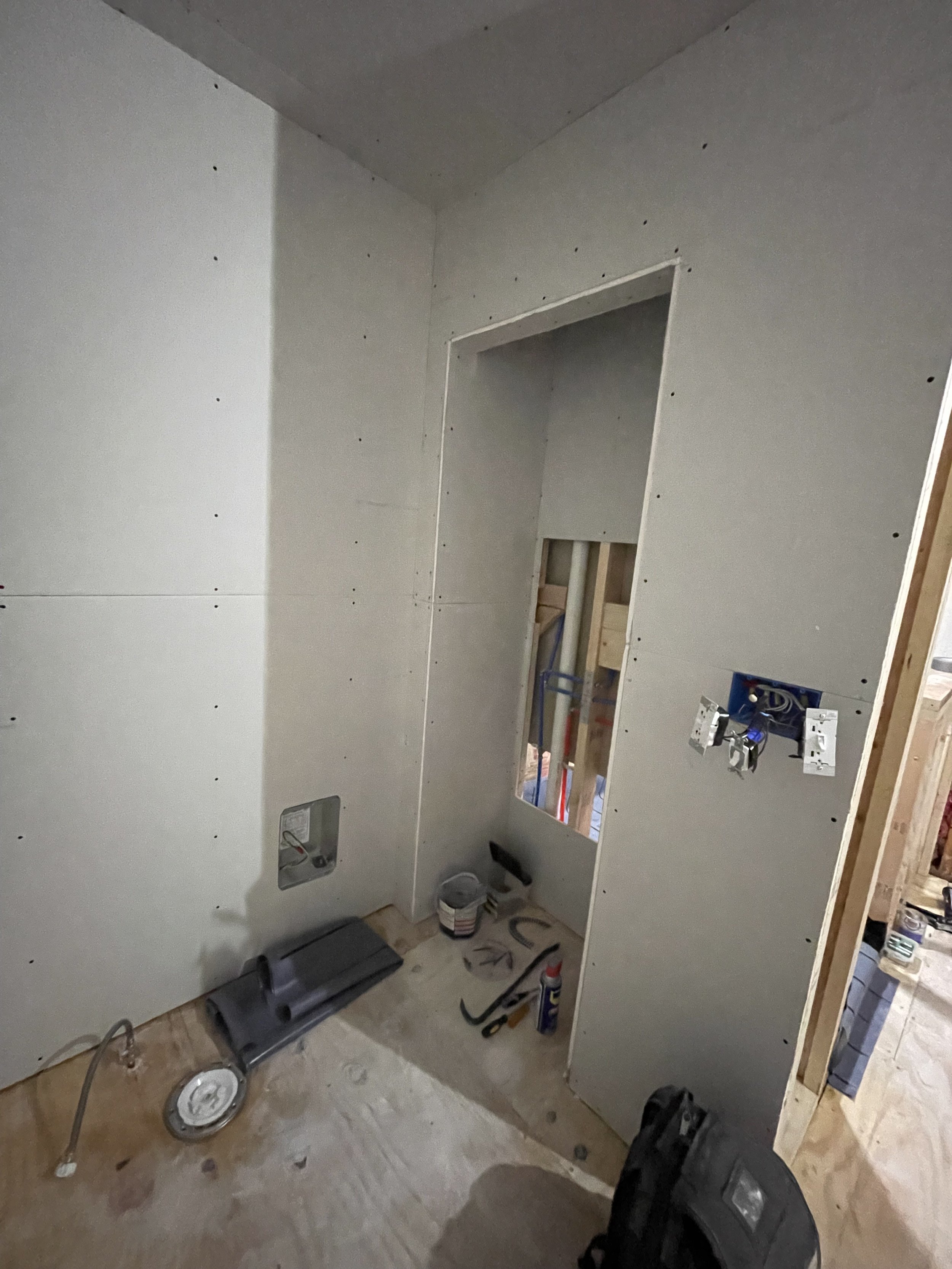 Bathroom under construction with drywall installed, electrical wiring, and plumbing fixtures in progress.