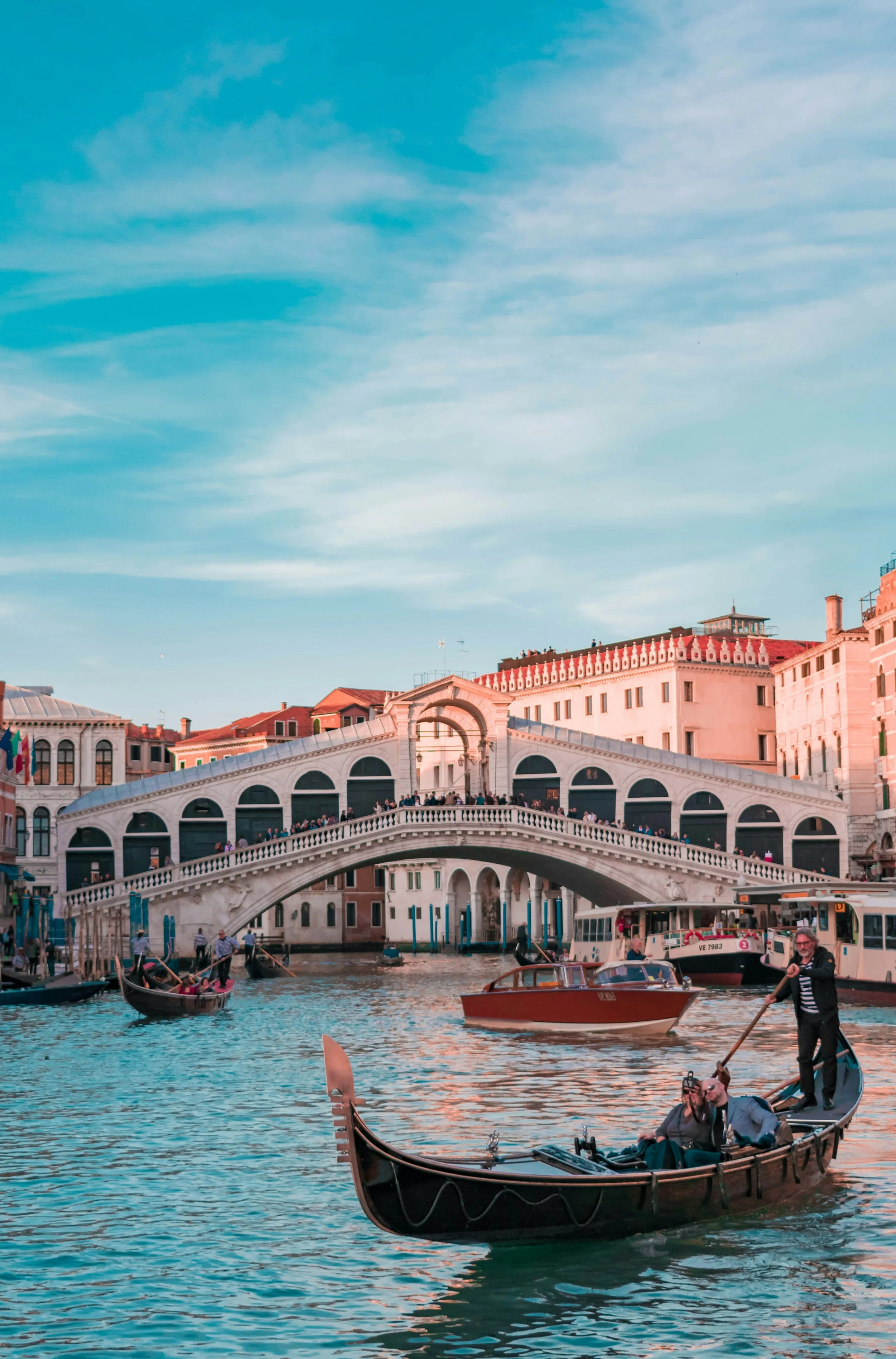 Gondola on a canal in Venice, Italy, with the Rialto Bridge and historic buildings in the background during a clear day.