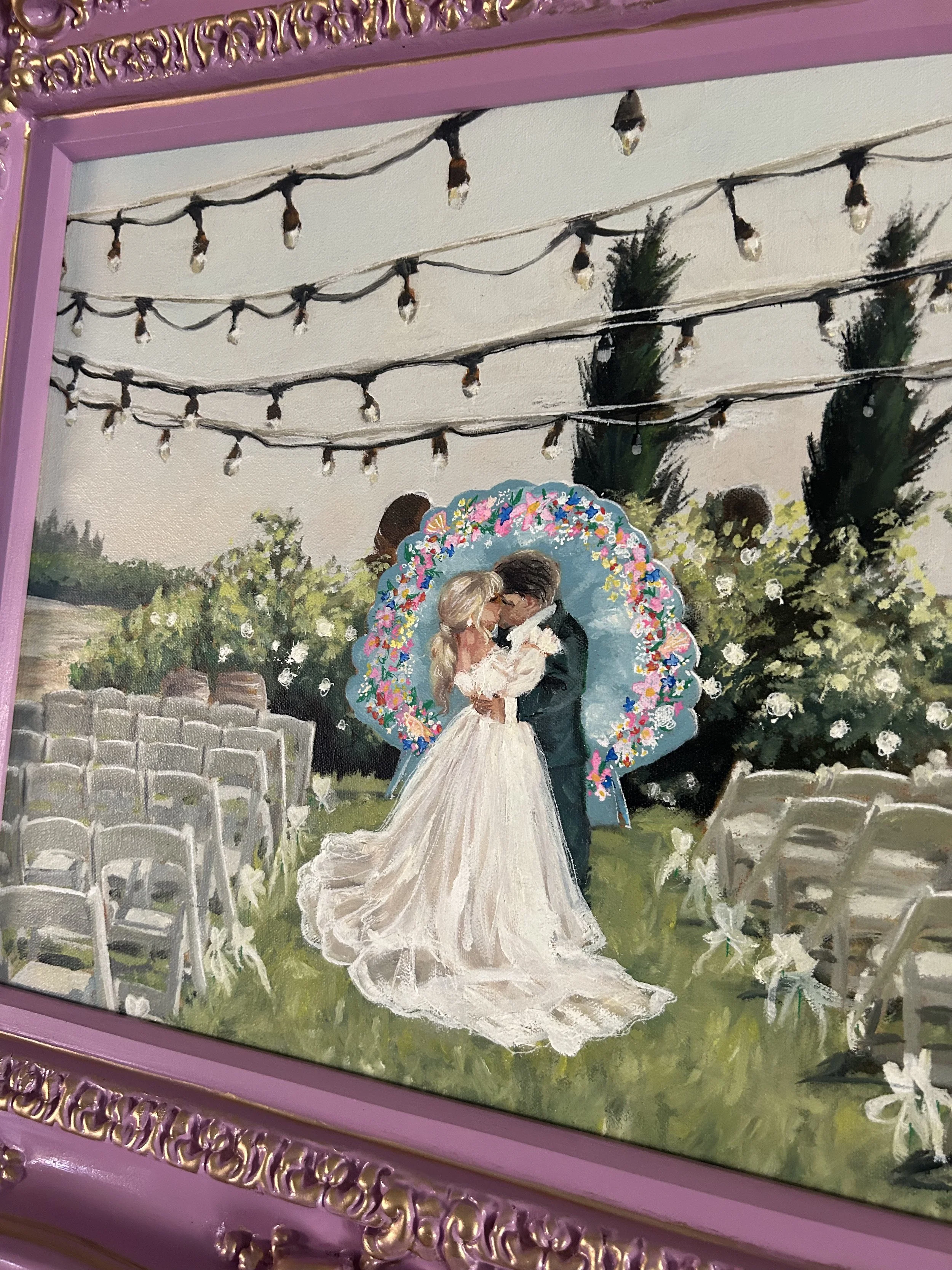 Live wedding painting of a couple kissing at their wedding ceremony outdoors, surrounded by white chairs, a floral arch, string lights, and greenery, all within a purple ornate frame.