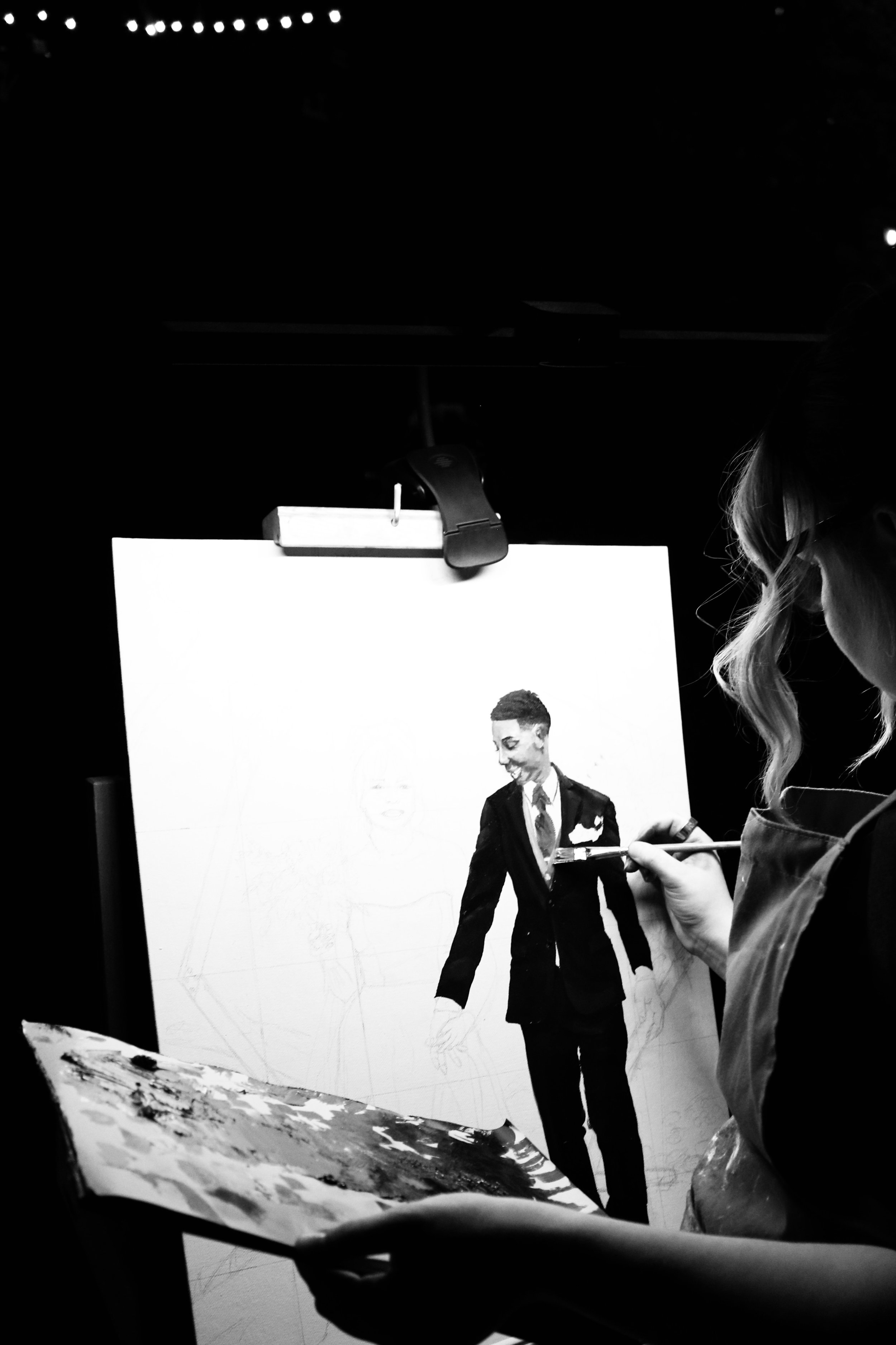 Anna Flores painting a realistic portrait of a man in a tuxedo on a large canvas outdoors, while the artist's face is not visible.