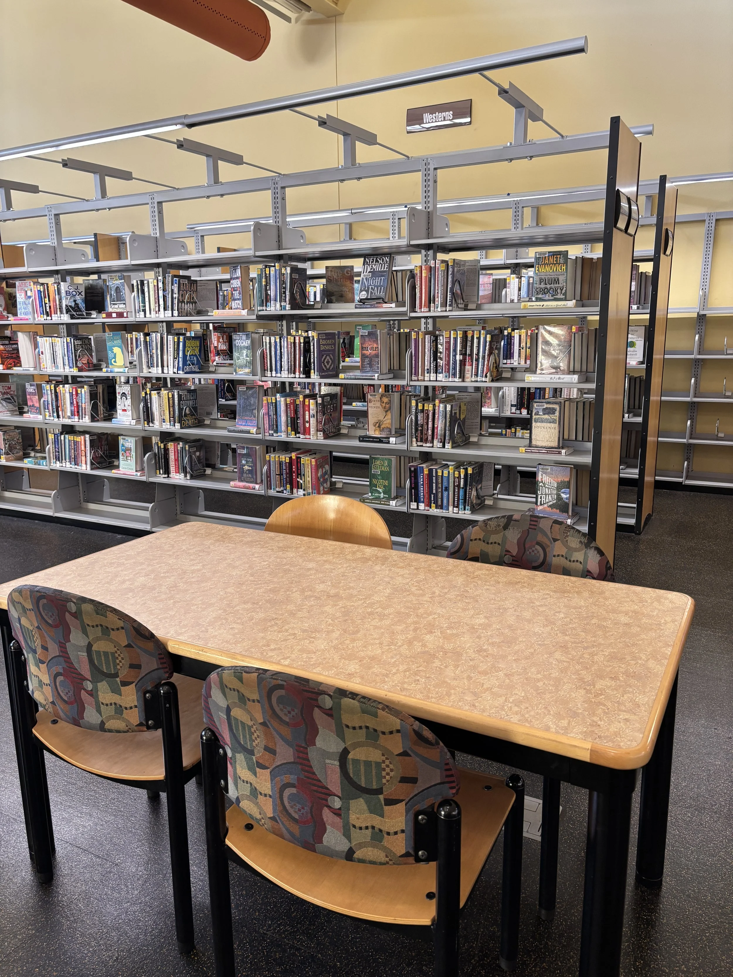 A library with a table and chairs in the foreground and bookshelves in the background.
