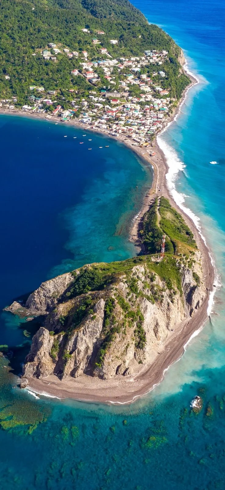 A coastal town with a beach, houses on a hillside, and a rocky peninsula with a lighthouse.