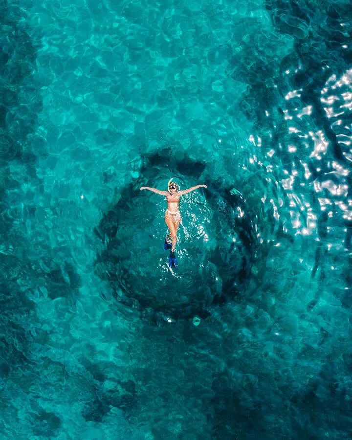 A woman in a bikini and snorkeling gear floating in clear blue water, enjoying a swim.