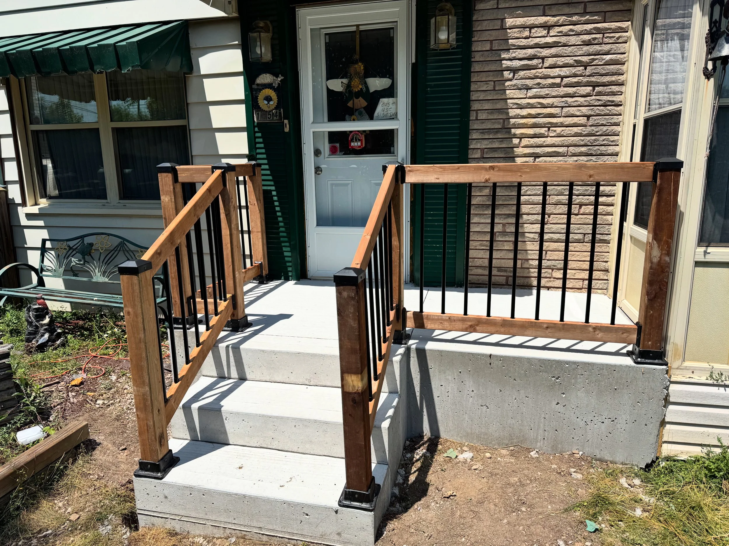 Front porch with newly installed wooden and metal railing on concrete stairs