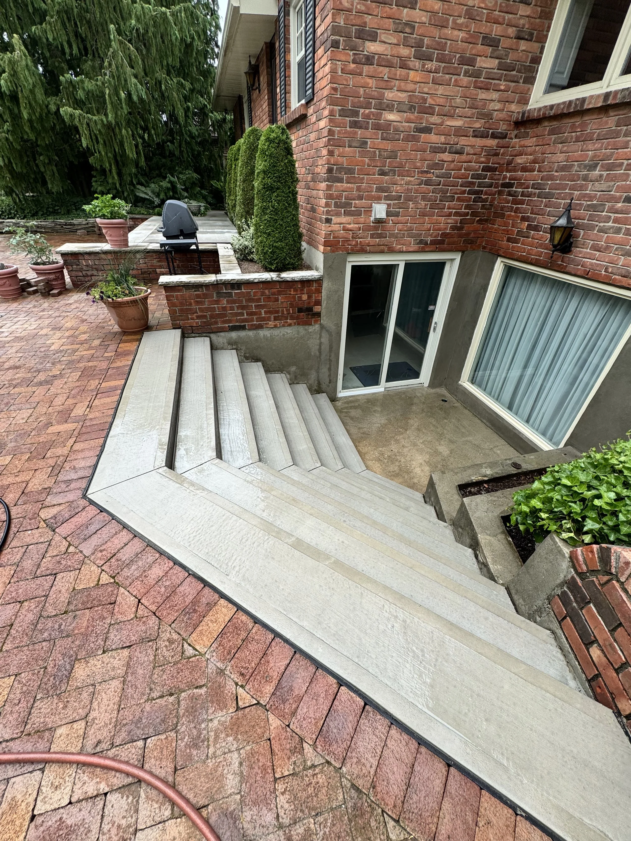 View of outdoor patio with brick and concrete stairs leading to basement entrance